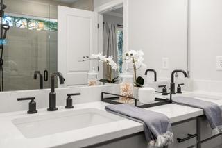 Modern master bathroom in The Washington H townhome featuring double white sinks, black faucets, quartz vanity, orchids, and glass shower