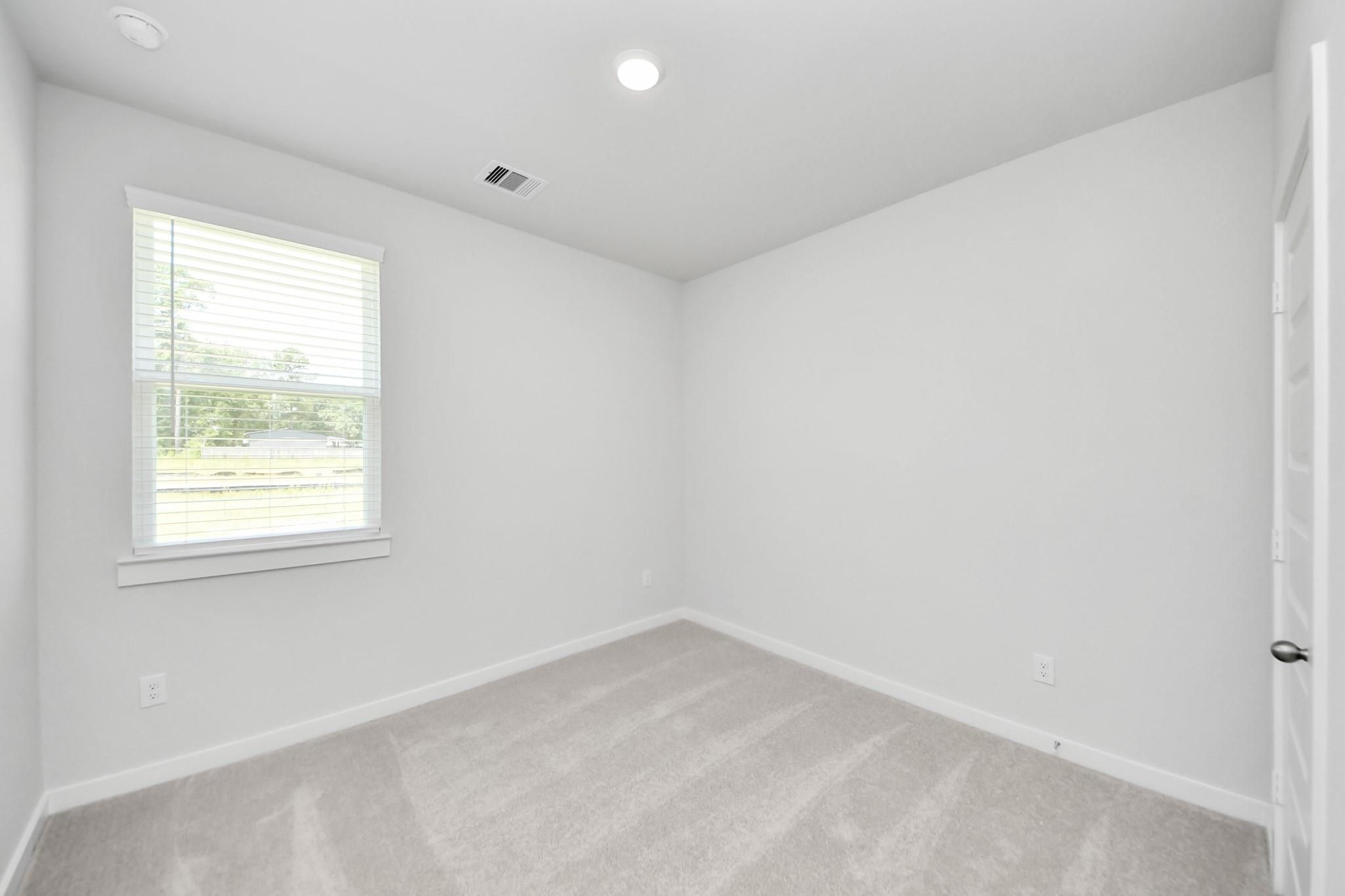 Bright, carpeted bedroom with neutral walls and a window in The Frio F floor plan at Liberty Estates, Cleveland, Texas.