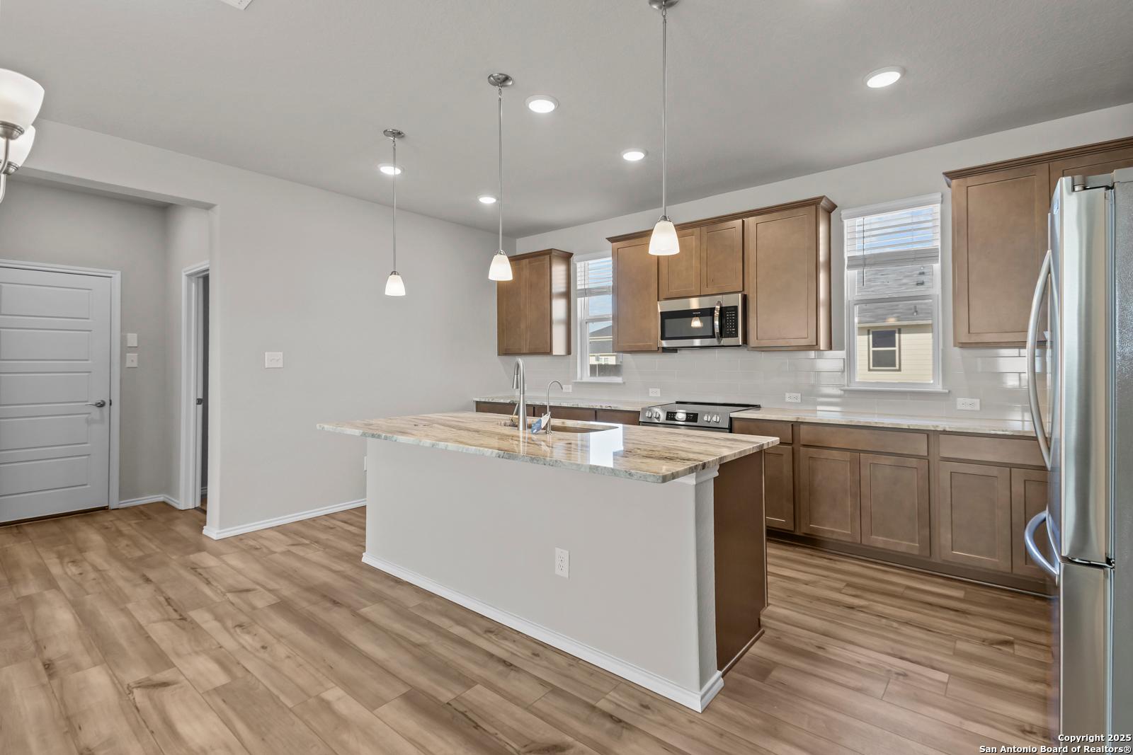 Modern kitchen with granite island, stainless appliances, wood cabinets in Davidson Homes The Collin B, Seguin TX