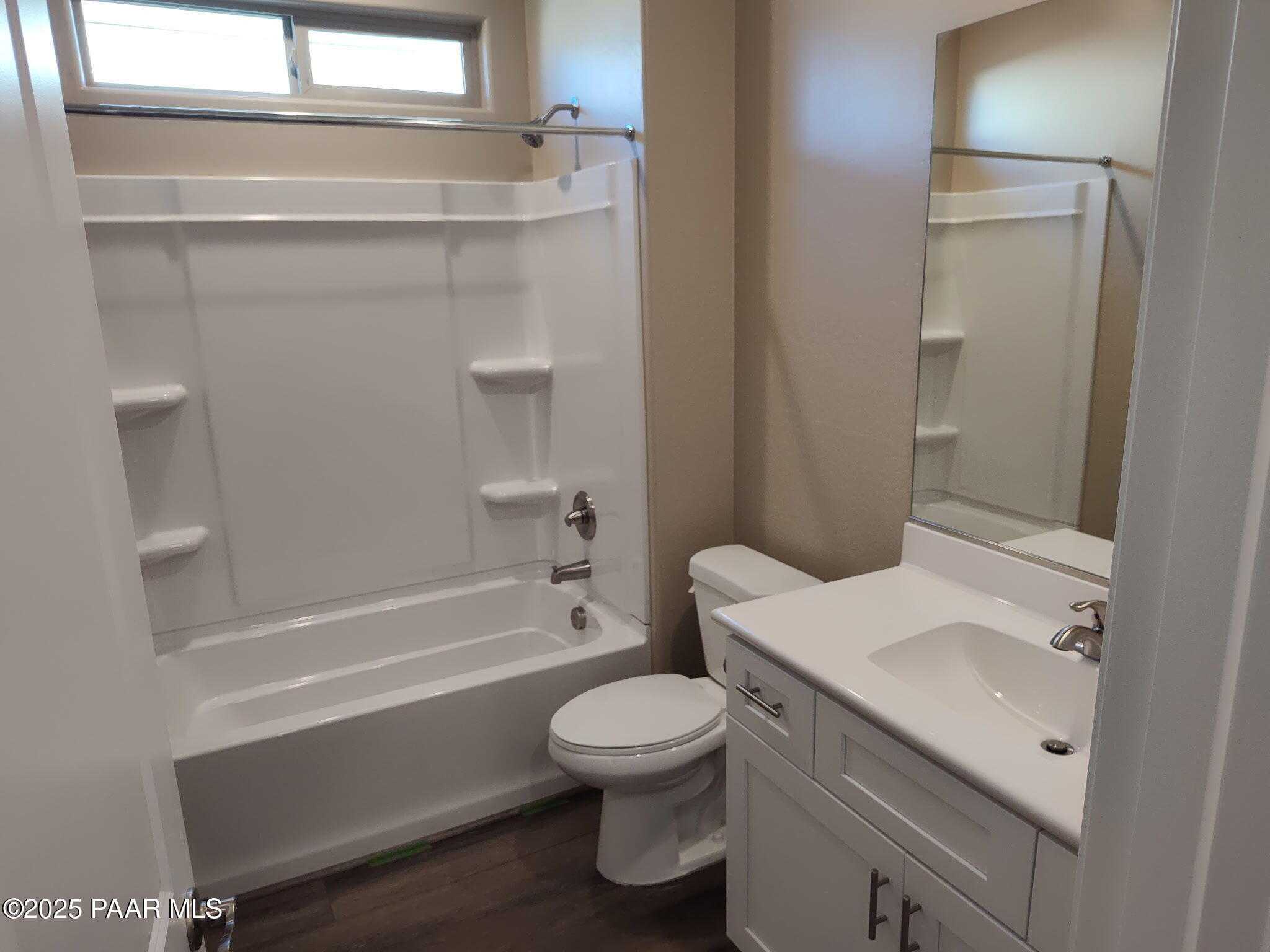 Modern guest bathroom featuring tub-shower combo, white vanity, mirror, and wood flooring in Davidson Homes The Inspiration A, Prescott Valley, Arizona