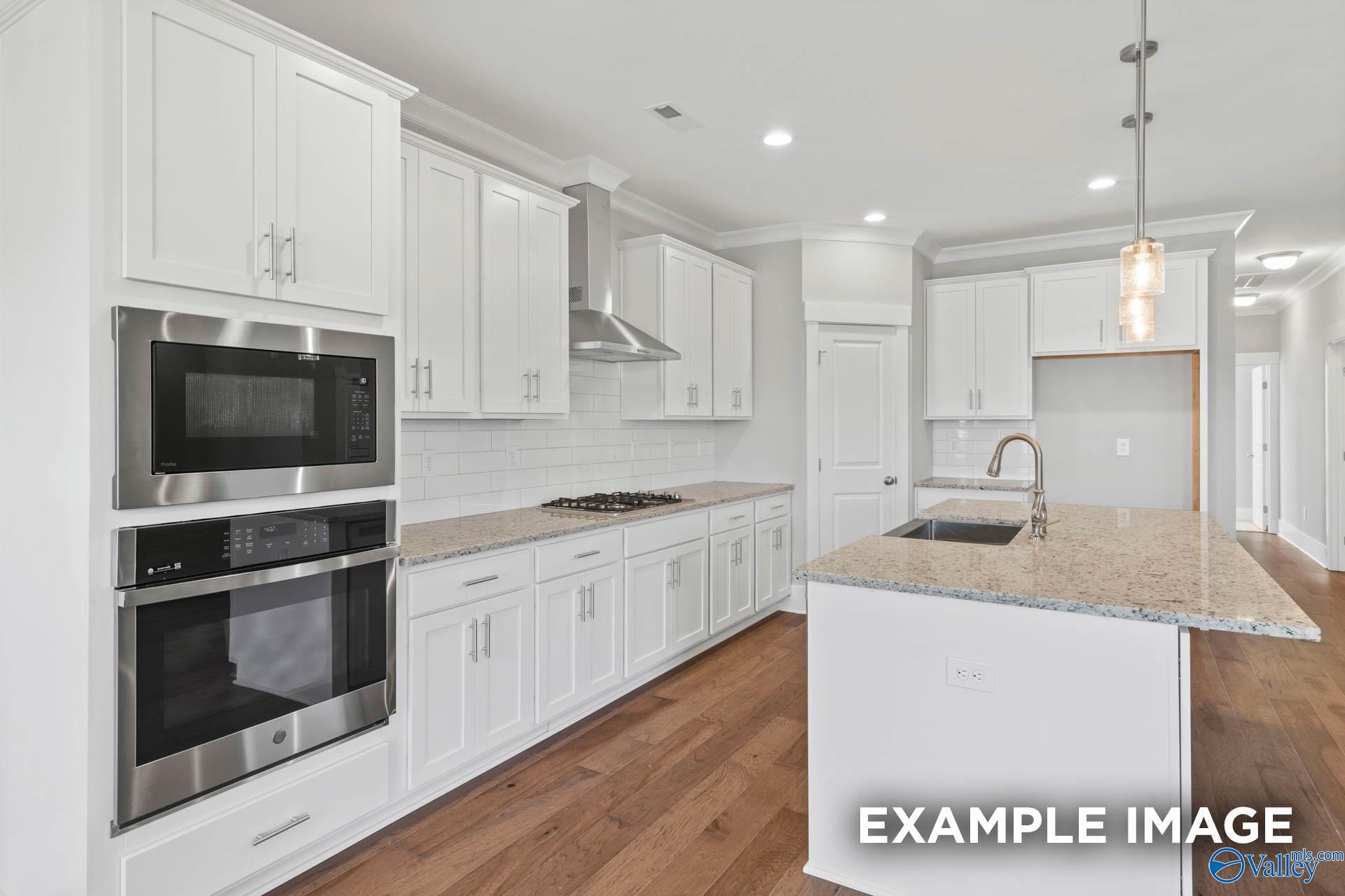 Modern kitchen with white cabinets, granite island, and stainless appliances in The Rockford floor plan, Cain Park, Hartselle.