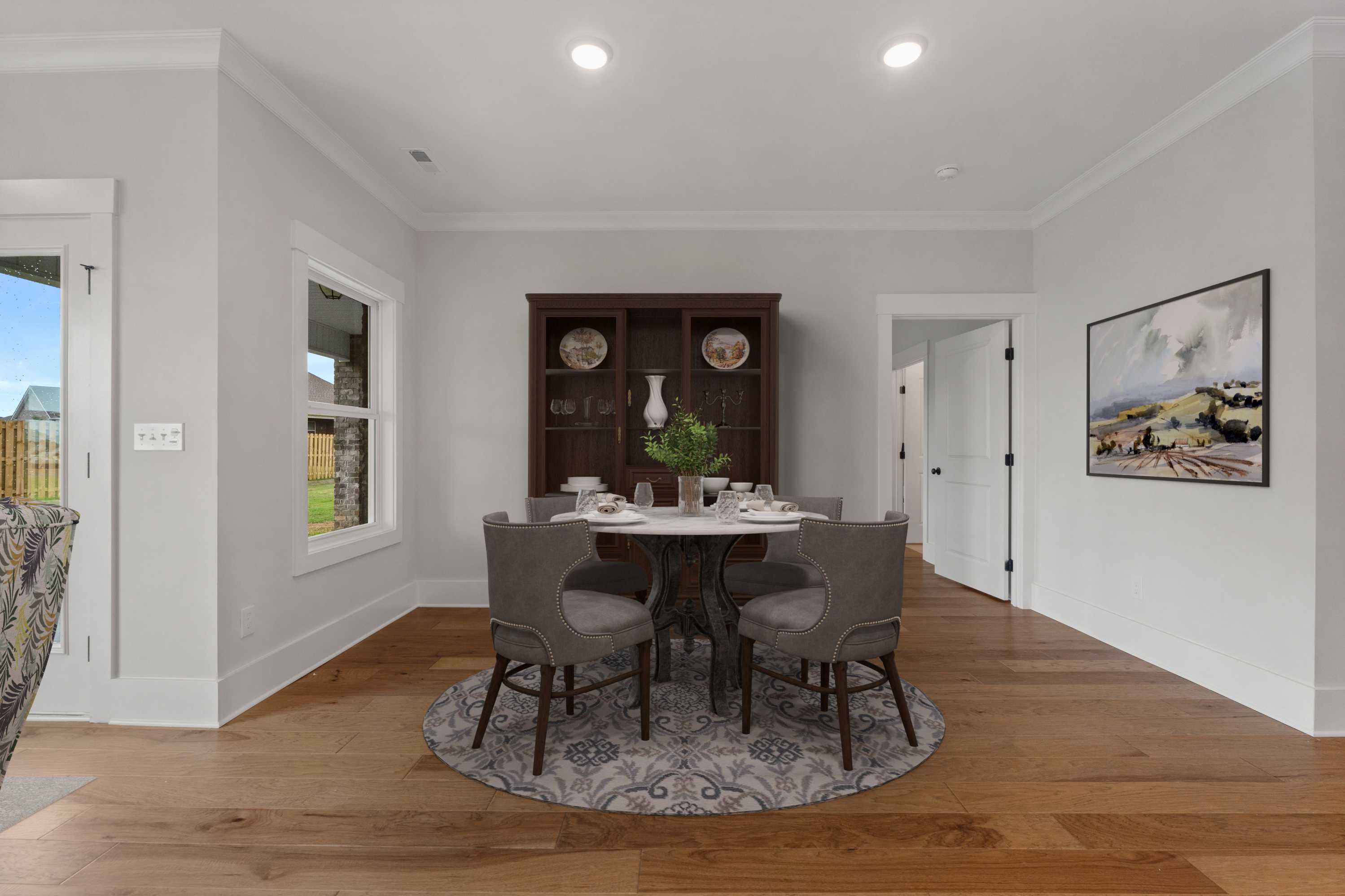 Elegant dining room at The Villas at Barnett's Crossing in Madison, Alabama with round table, upholstered chairs, hardwood floors, and buffet cabinet