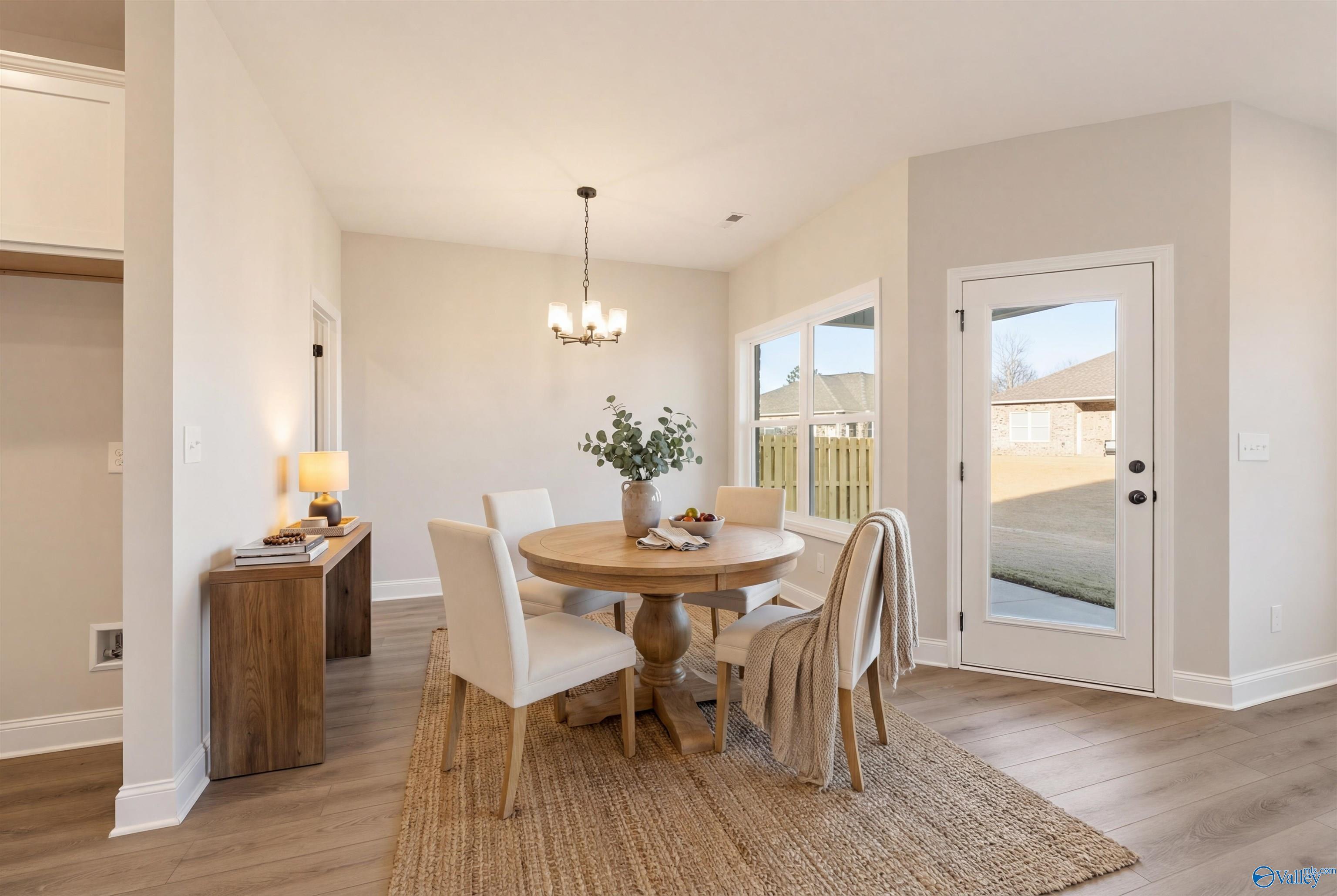 Elegant dining room with round wooden table, white chairs, chandelier, and French doors to backyard in The Daphne D by Davidson Homes, Arab, Alabama