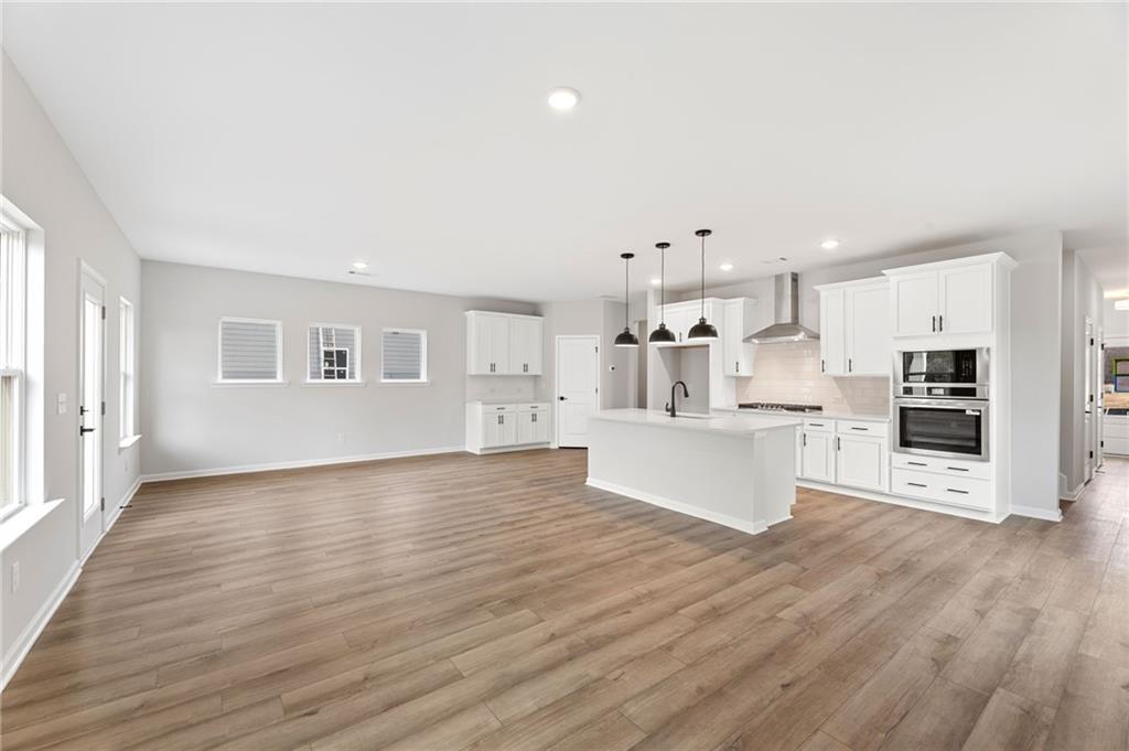 Modern white kitchen island with stainless appliances, pendant lights, and hardwood floors in The Rabun C, Winder, GA