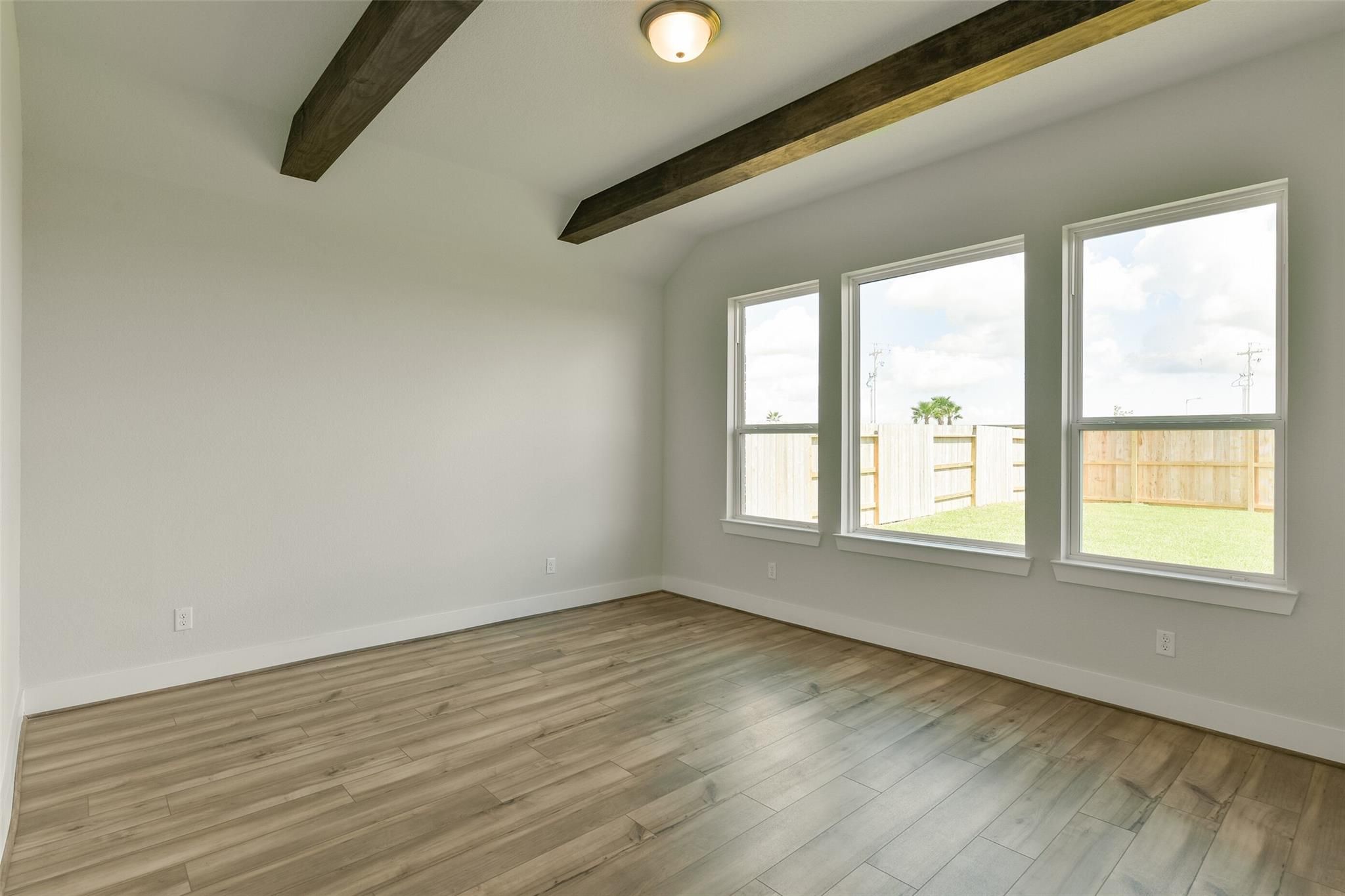 Bright living room with vaulted wooden beam ceiling, hardwood floors, and large windows to fenced backyard in Davidson Homes The Edward A, Lago Mar, Texas City