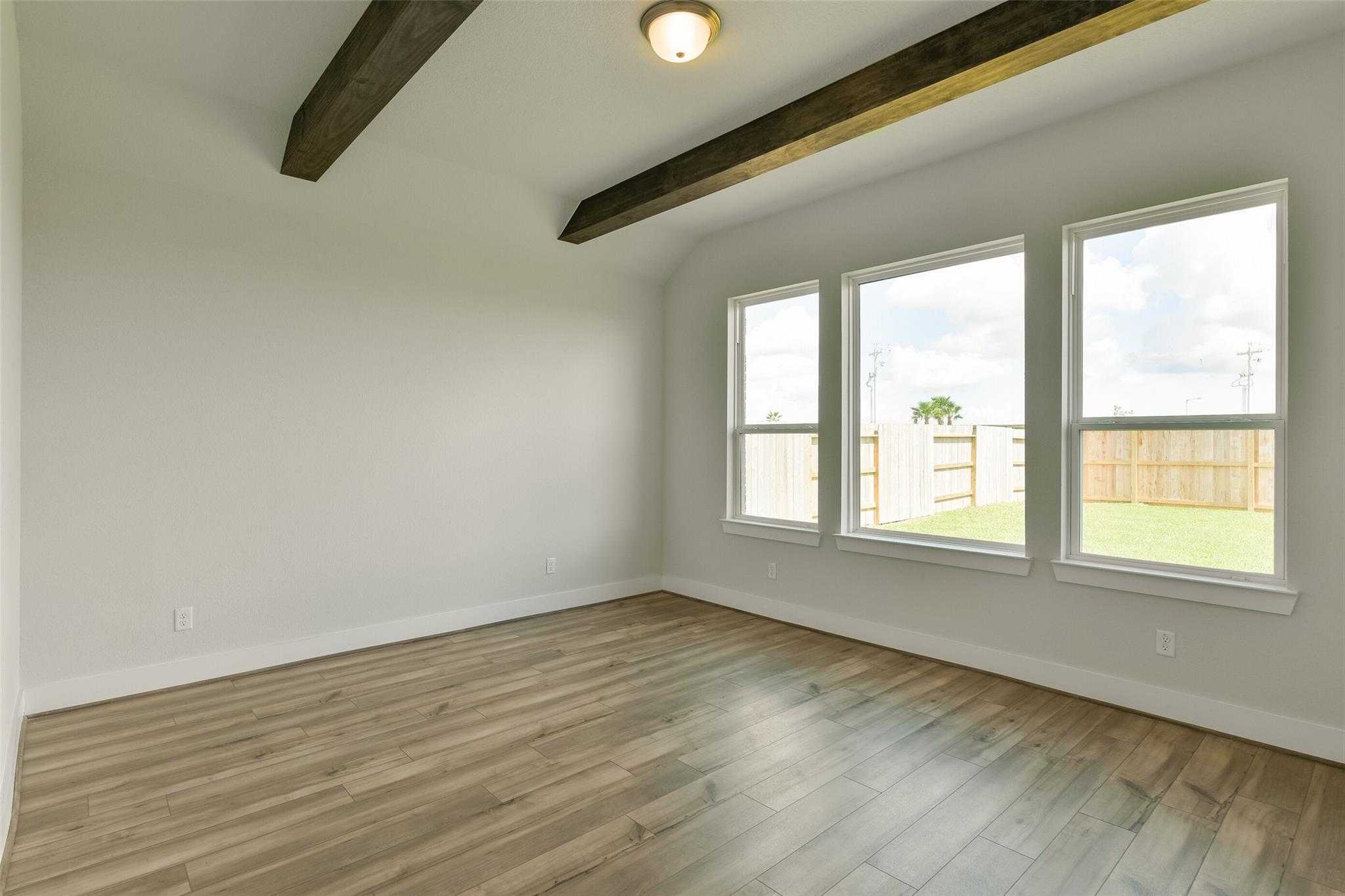 Bright living room with vaulted wooden beam ceiling, hardwood floors, and large windows to fenced backyard in Davidson Homes The Edward A, Lago Mar, Texas City
