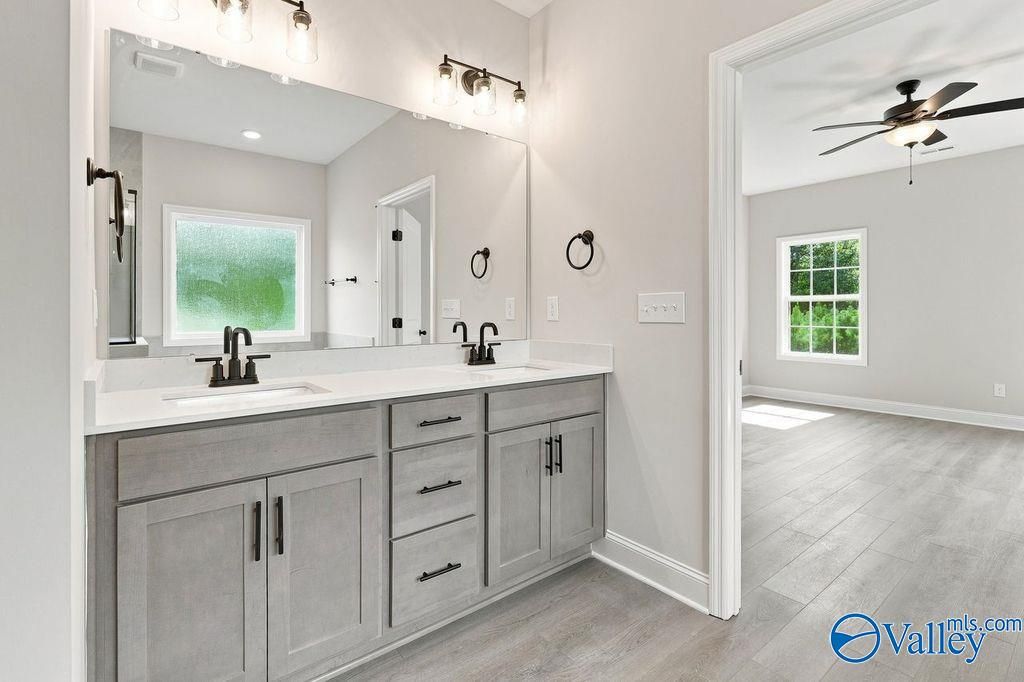 Dual vanity bathroom with gray cabinets, large mirror, and luxury vinyl plank flooring in Davidson Homes' The Rockford, Hartselle, Alabama