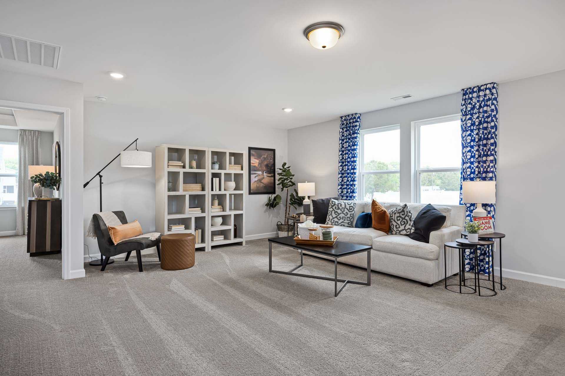 Spacious living room at Beverly Place in Four Oaks NC with beige sofa, bookshelves, blue curtains, and neutral tones