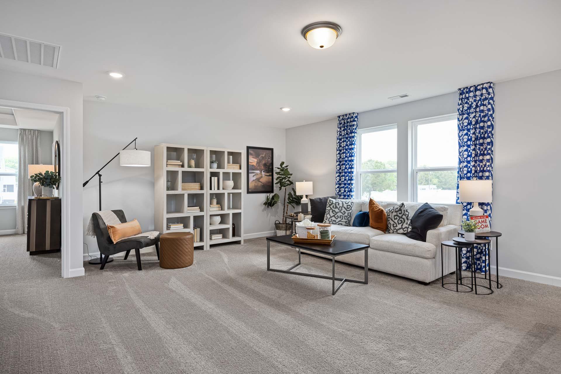 Spacious living room at Beverly Place in Four Oaks NC with beige sofa, bookshelves, blue curtains, and neutral tones