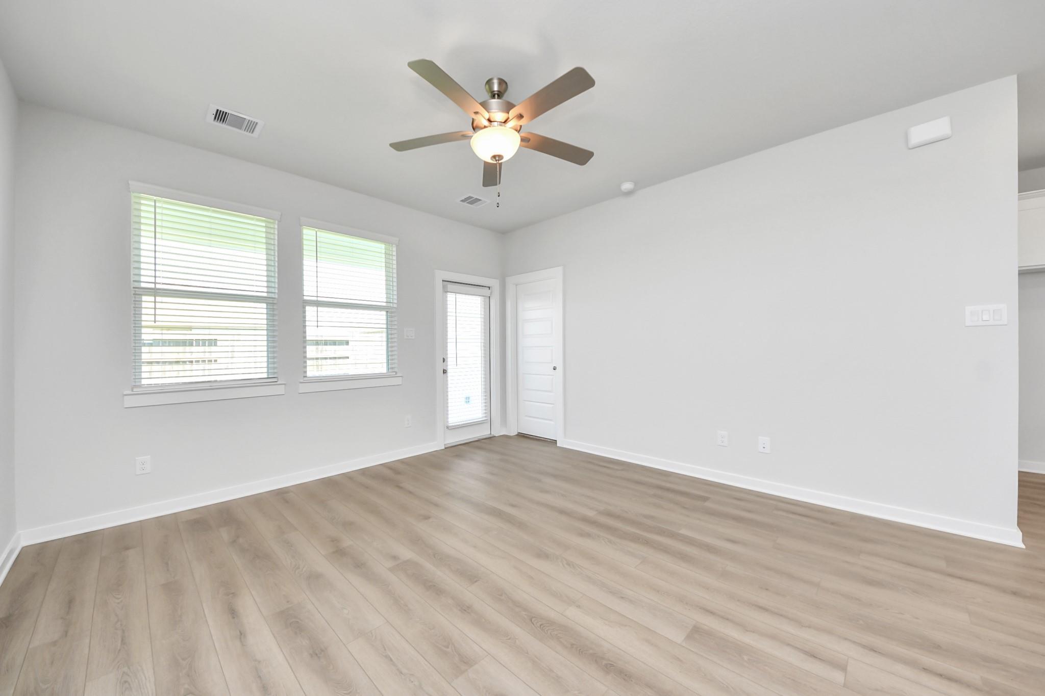 Bright empty room with wood-look flooring, ceiling fan, and blinds in Davidson Homes The Costa A, Beasley, Texas