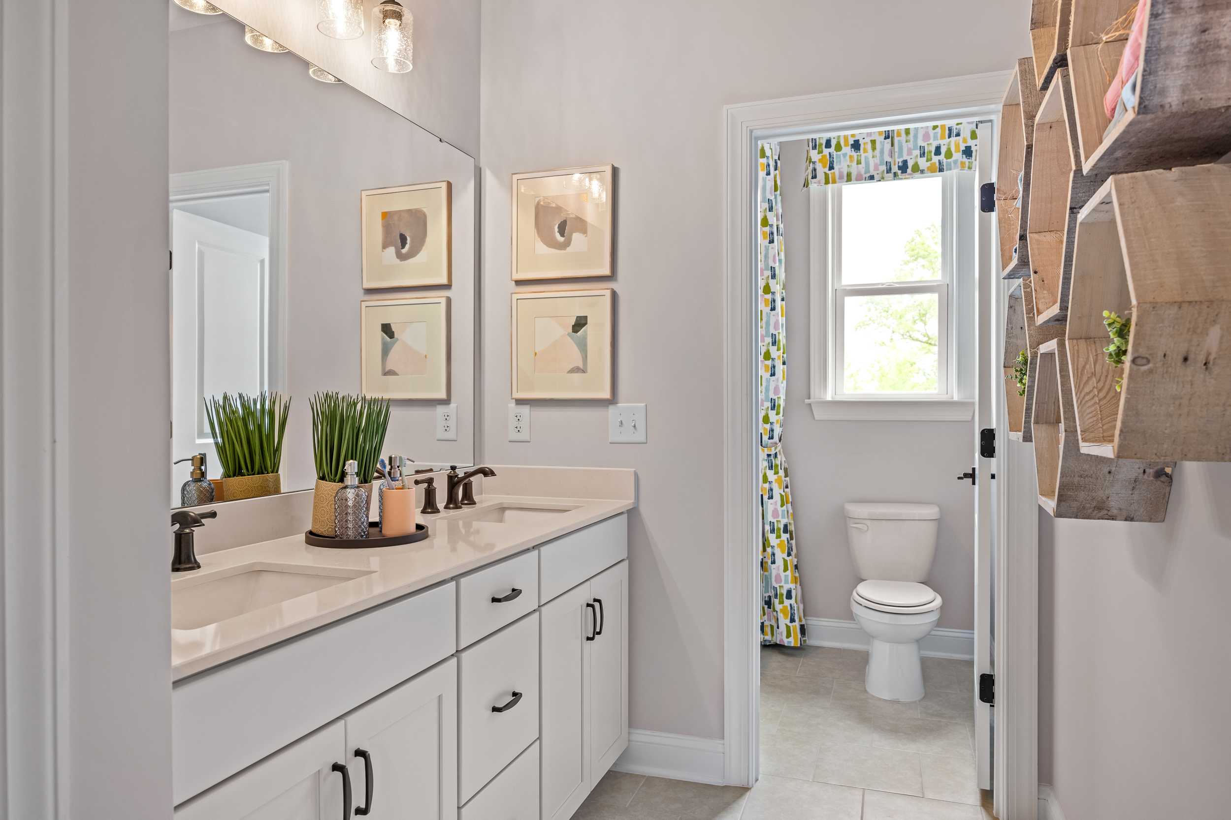 Spacious bathroom at Laneridge Estates in Raleigh NC with double white vanity, large mirror, abstract art, potted plants, and yellow curtained door
