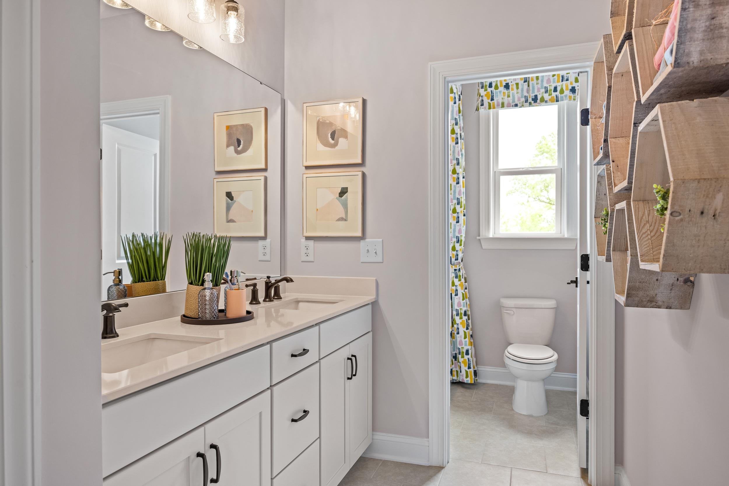 Spacious bathroom at Laneridge Estates in Raleigh NC with double white vanity, large mirror, abstract art, potted plants, and yellow curtained door