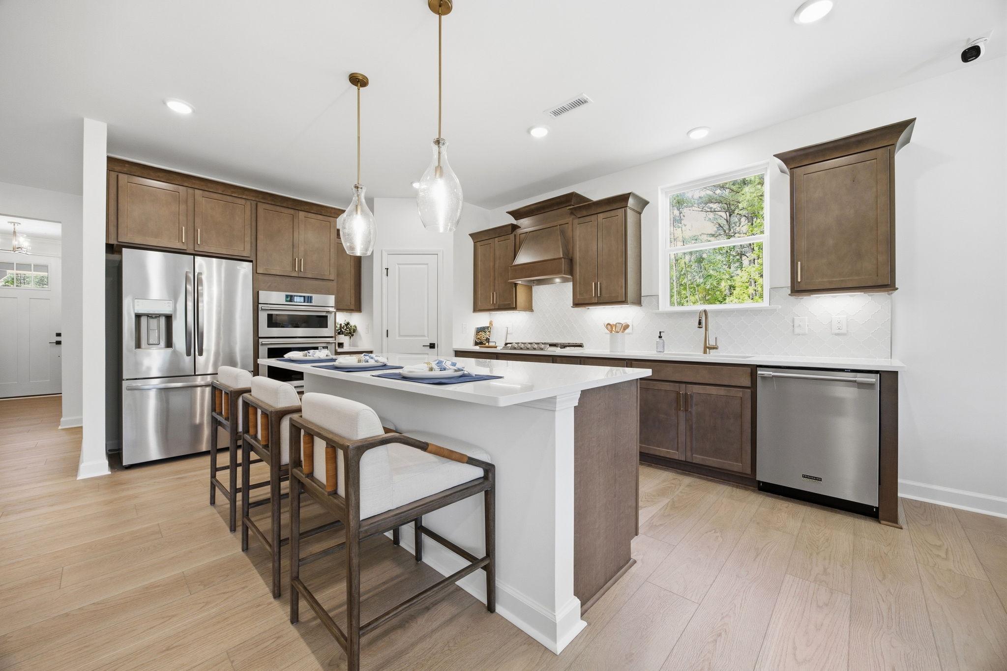 Modern kitchen at Sage on North Main in Wake Forest NC featuring large quartz island, shaker cabinets, stainless appliances, and pendant lights