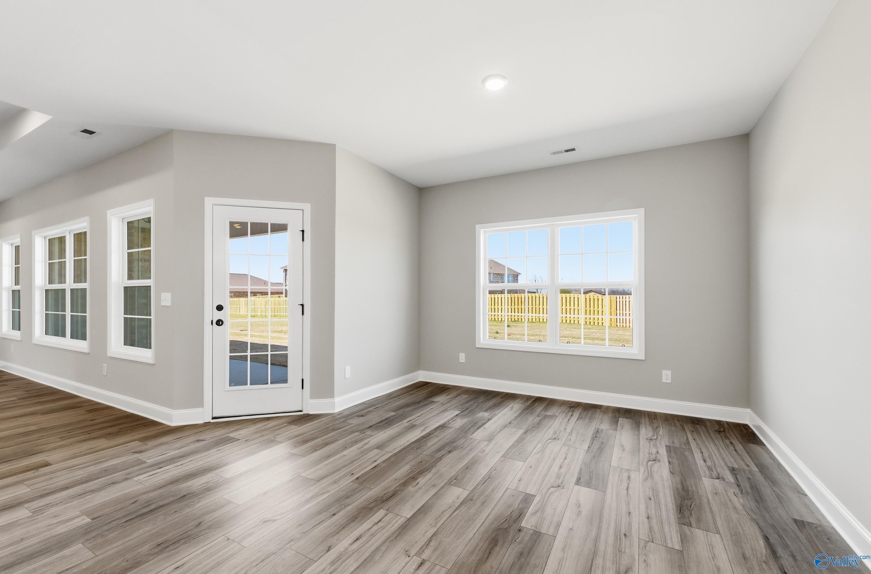 Spacious family room with gray walls, large windows, glass door to fenced backyard, and hardwood floors in Davidson Homes The Rockford, Harvest AL