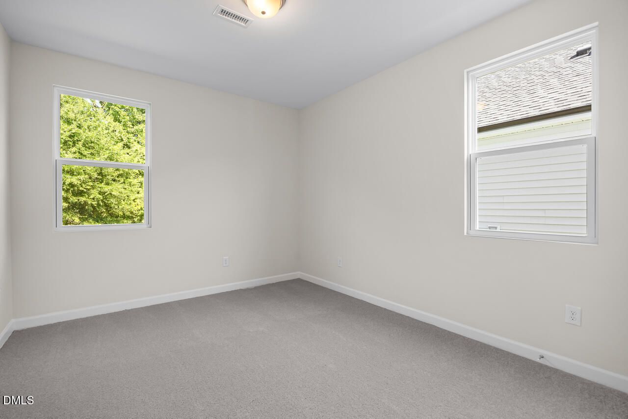 Bright empty bedroom with neutral walls, carpet, and two windows in Davidson Homes' The Willow C, Zebulon, North Carolina
