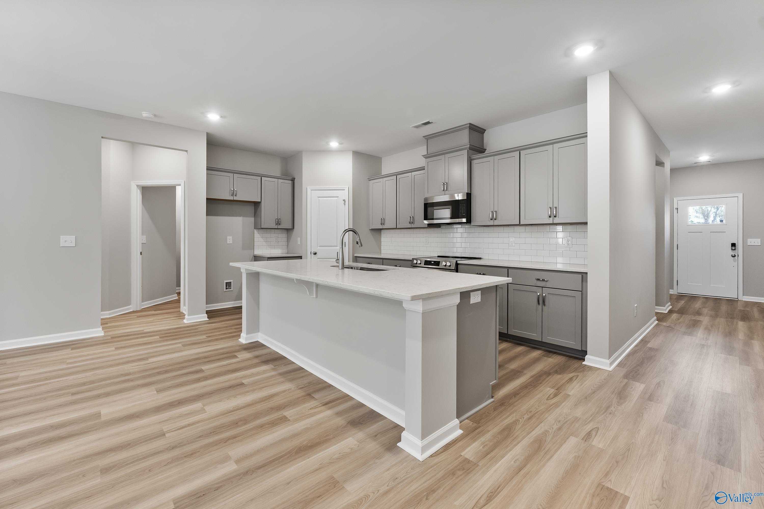 Modern gray kitchen with large center island, stainless appliances, and open layout in Evermore Homes The Grace, Madison, Alabama