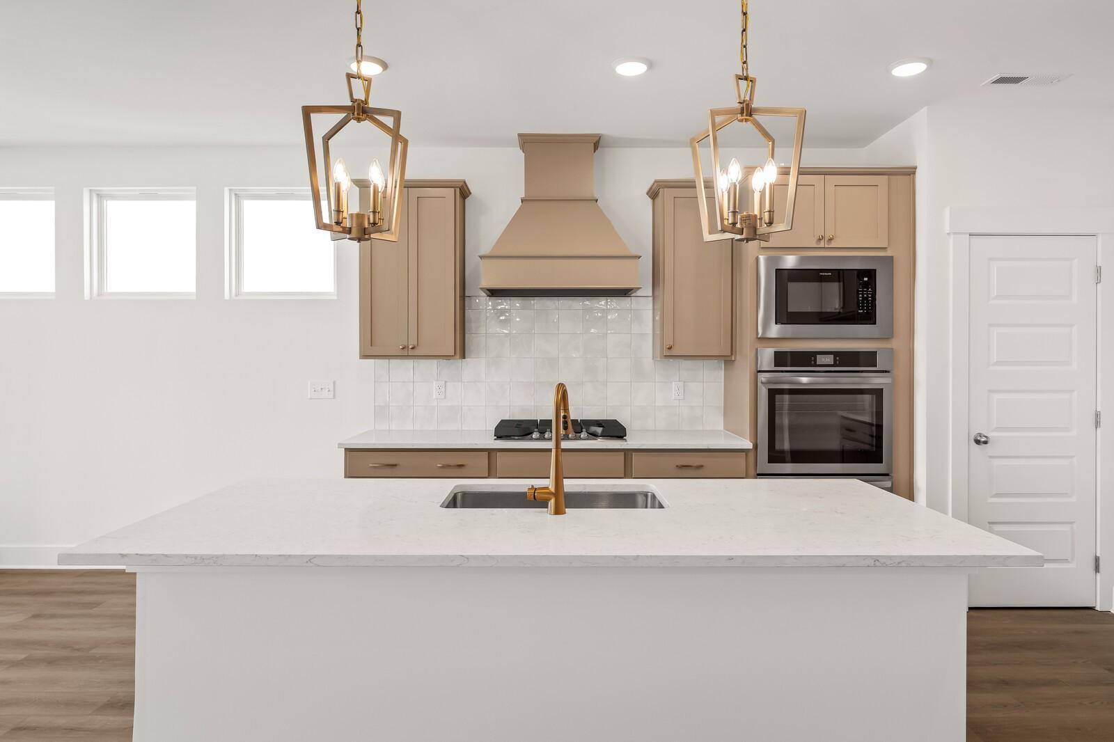 Spacious modern kitchen with white quartz island, brass pendants, subway backsplash, stainless double oven in Davidson Homes The Ash A, Gallatin TN