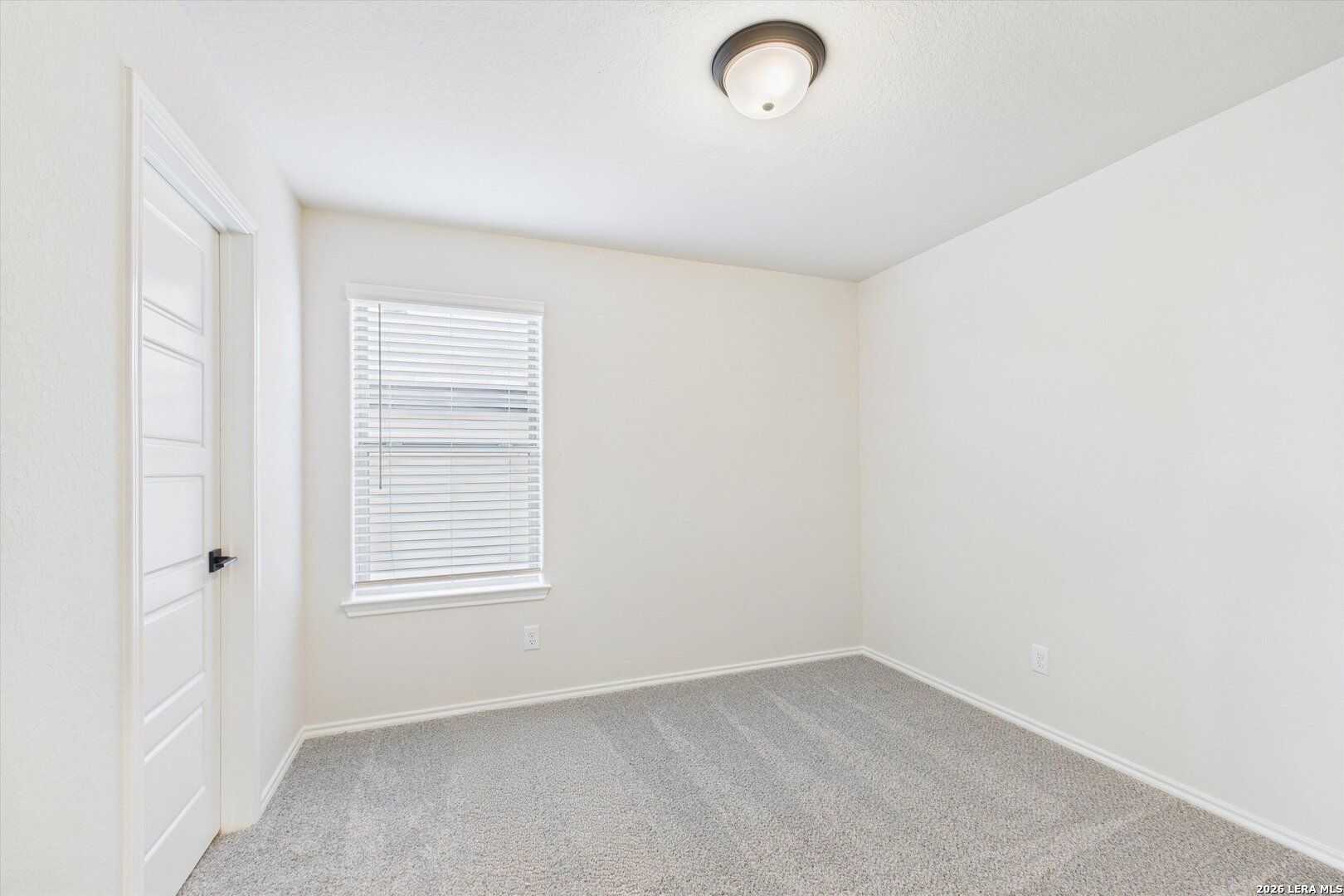 Bright empty secondary bedroom with neutral walls, gray carpet, window blinds, and ceiling light in Davidson Homes The Gillian B, San Antonio