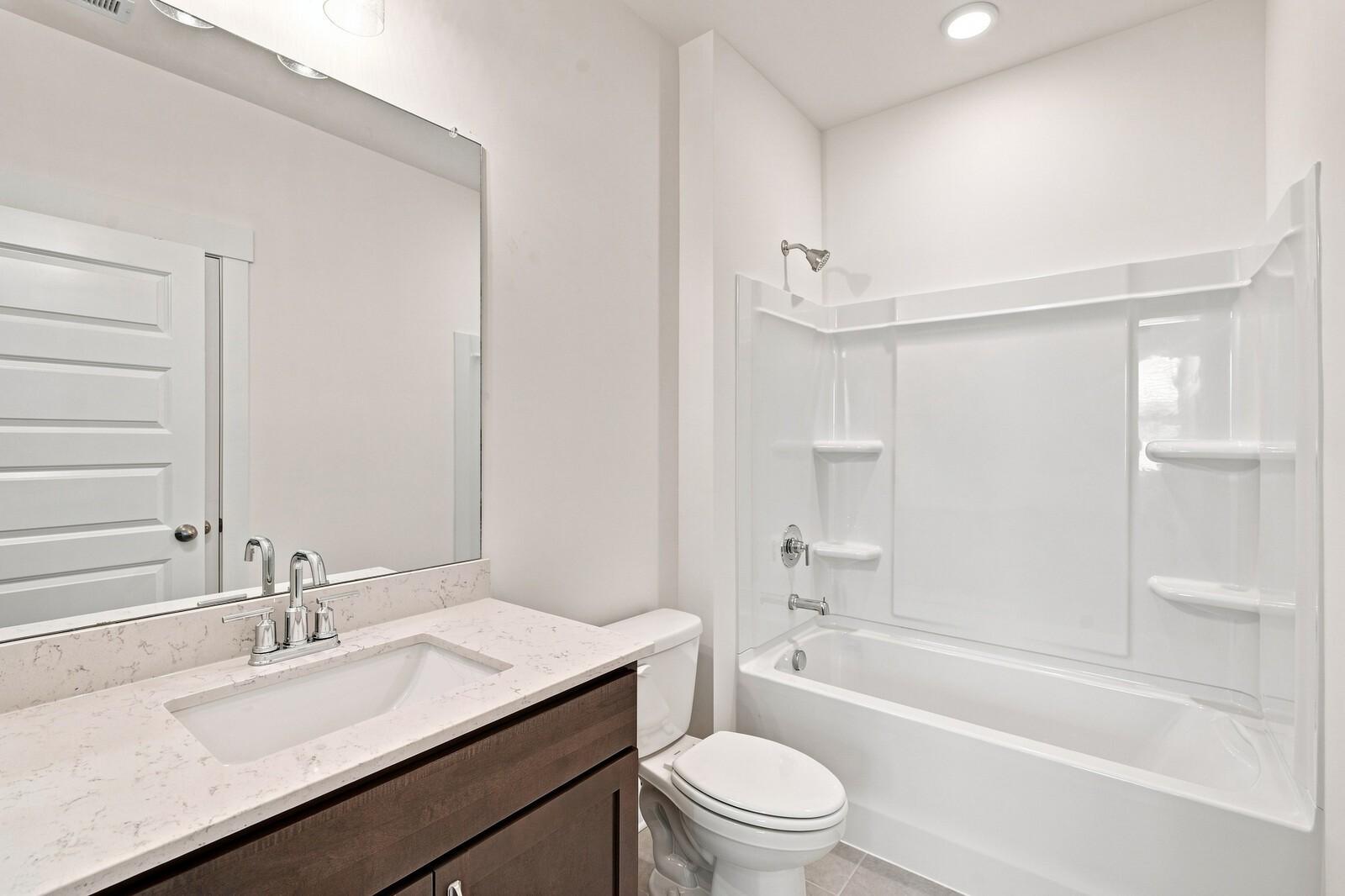 Bright bathroom with quartz vanity, wood cabinet, and tub shower combo in Davidson Homes The Willow C, Gallatin, TN