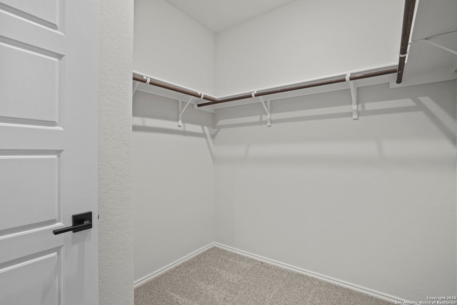 Spacious walk-in closet with white hanging rods and shelves in master suite of Davidson Homes The Douglas C, Hannah Heights, Seguin, Texas