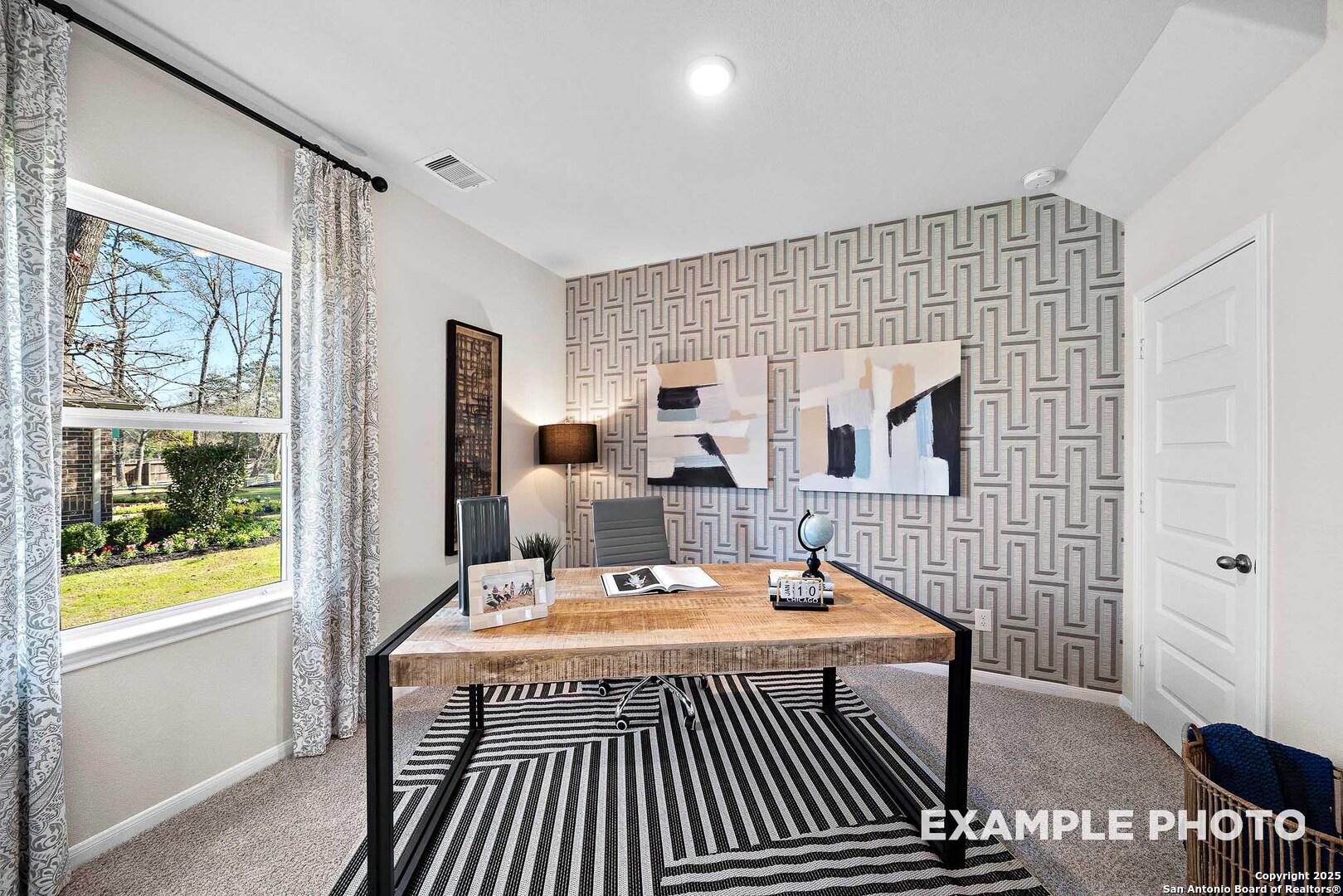 Modern home office with wooden desk, geometric wallpaper, abstract art, and window view of lush yard in Davidson Homes The San Marcos D, San Antonio