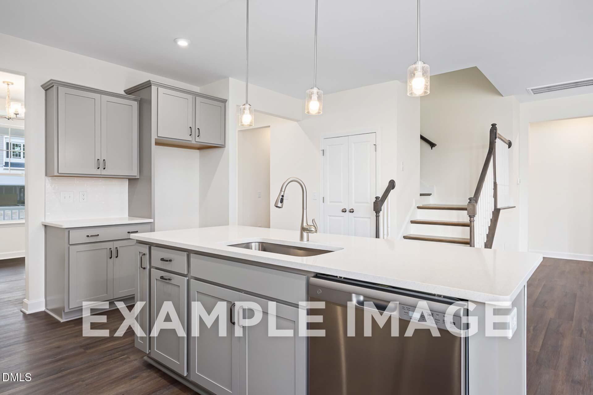 Open-concept kitchen with gray shaker cabinets, quartz island sink, stainless dishwasher, and pendant lights in The Ash B, Zebulon NC