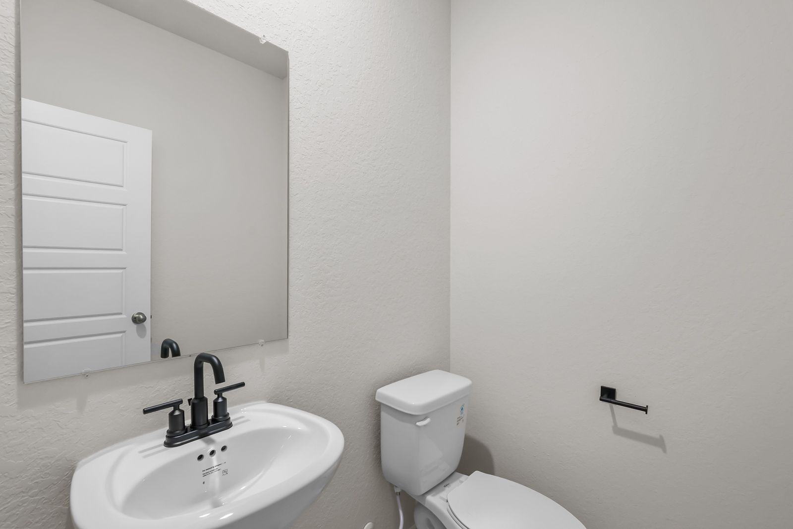 Modern powder room in The Sequoia C home design featuring a pedestal sink, black fixtures, and a sleek wall mirror.