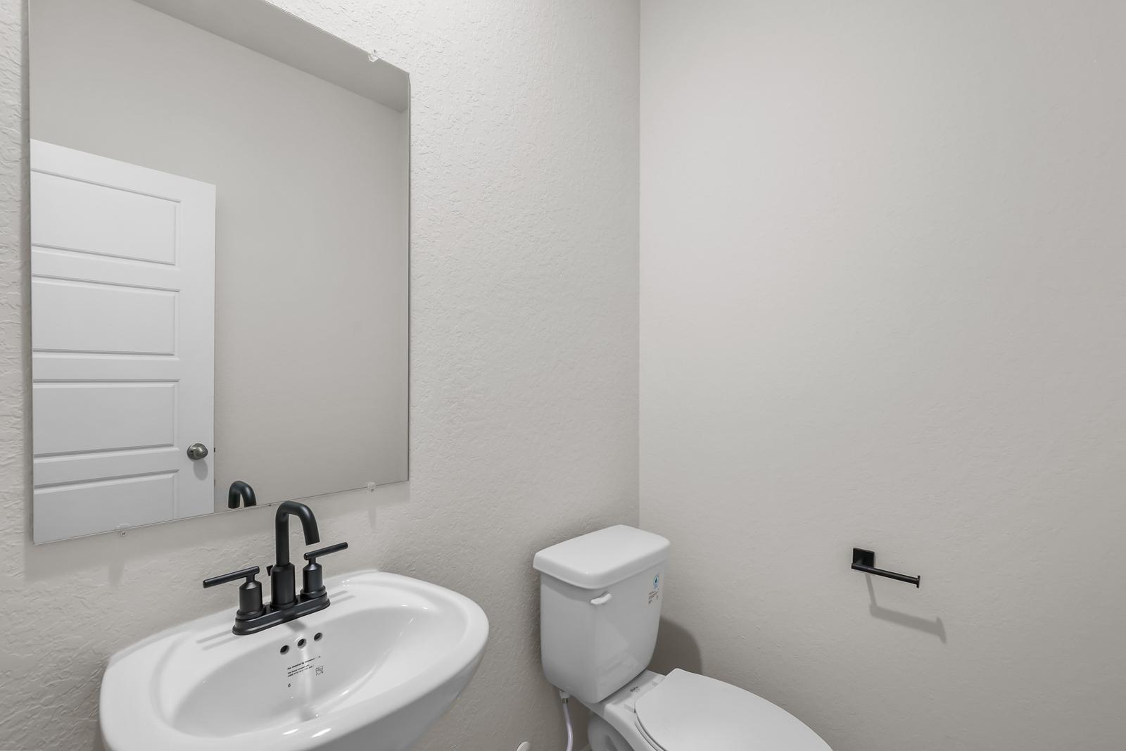 Modern powder room in The Sequoia C home design featuring a pedestal sink, black fixtures, and a sleek wall mirror.
