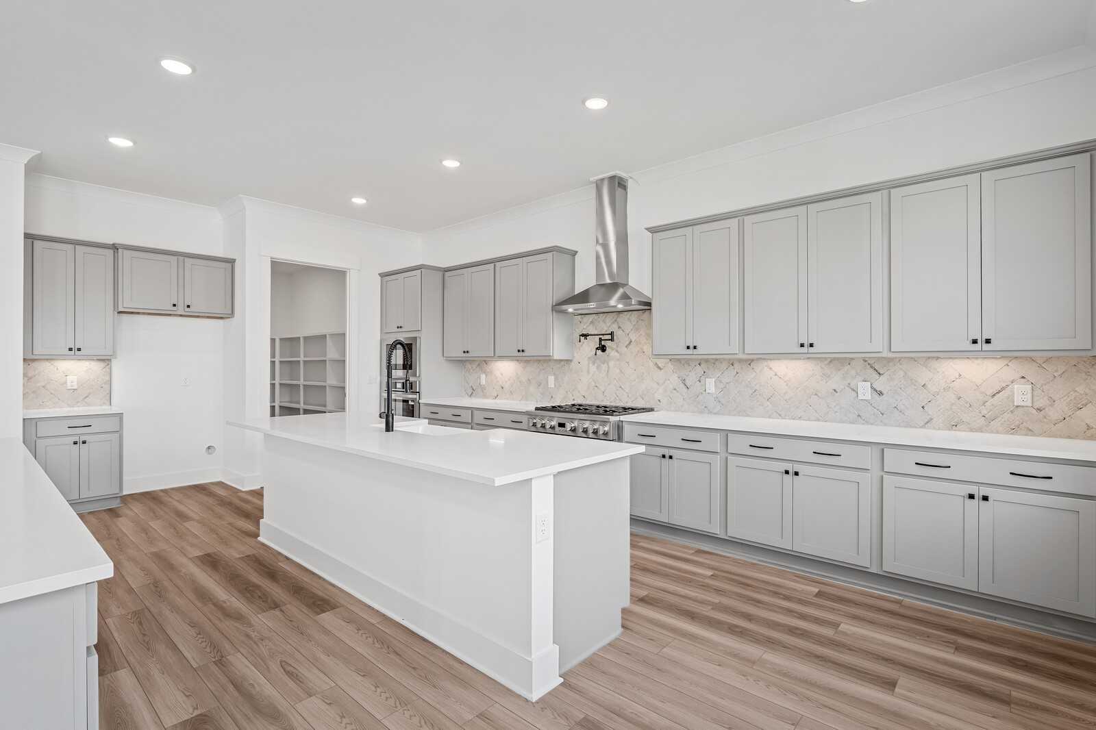 Modern kitchen with white quartz island, gray shaker cabinets, stainless steel range and subway tile backsplash in The Alston A, Murfreesboro, TN