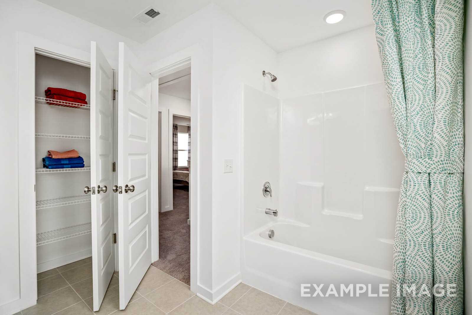 Modern bathroom in The Gordon B by Davidson Homes featuring white tub, teal shower curtain, and open linen closet with red towels