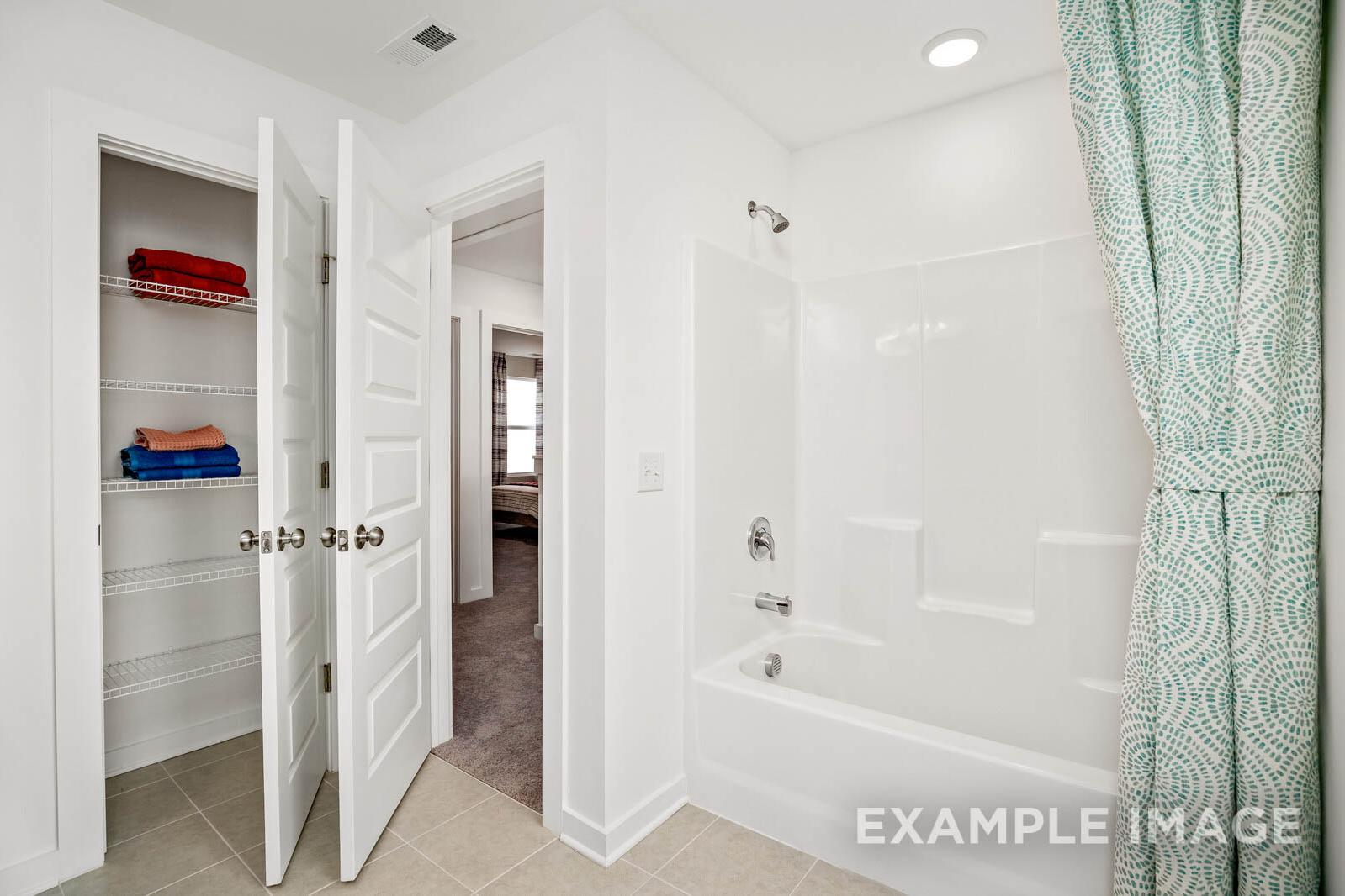 Bright white bathroom in The Gordon C featuring alcove tub with teal shower curtain and open linen closet with red towels