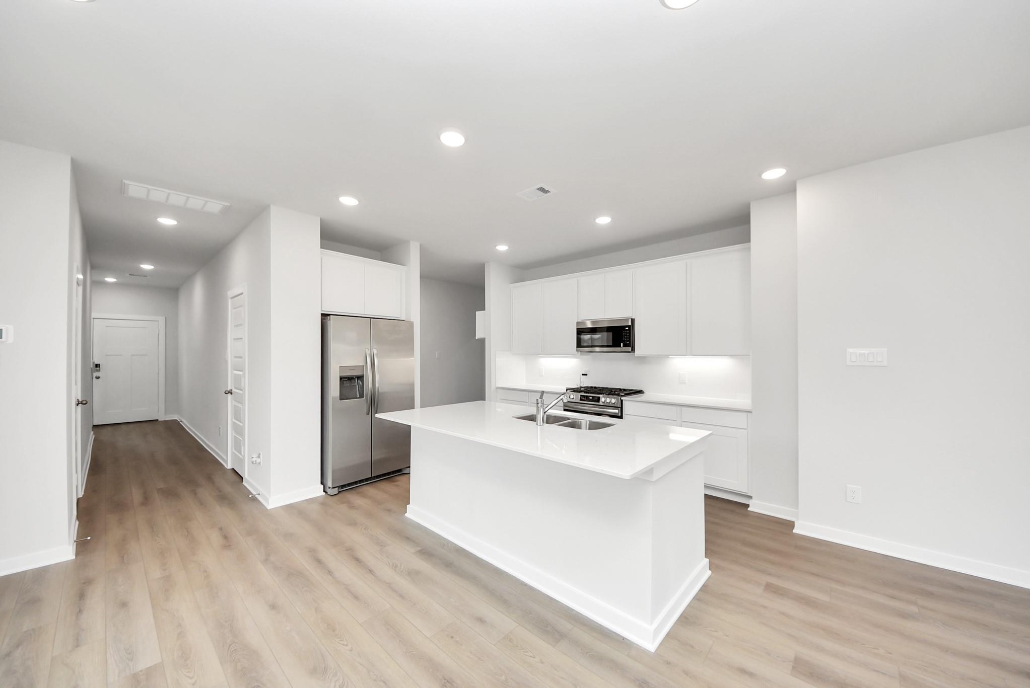 Modern white kitchen with island, stainless appliances, and wood-style flooring in The Blanco E at The Villages, Dayton, TX.
