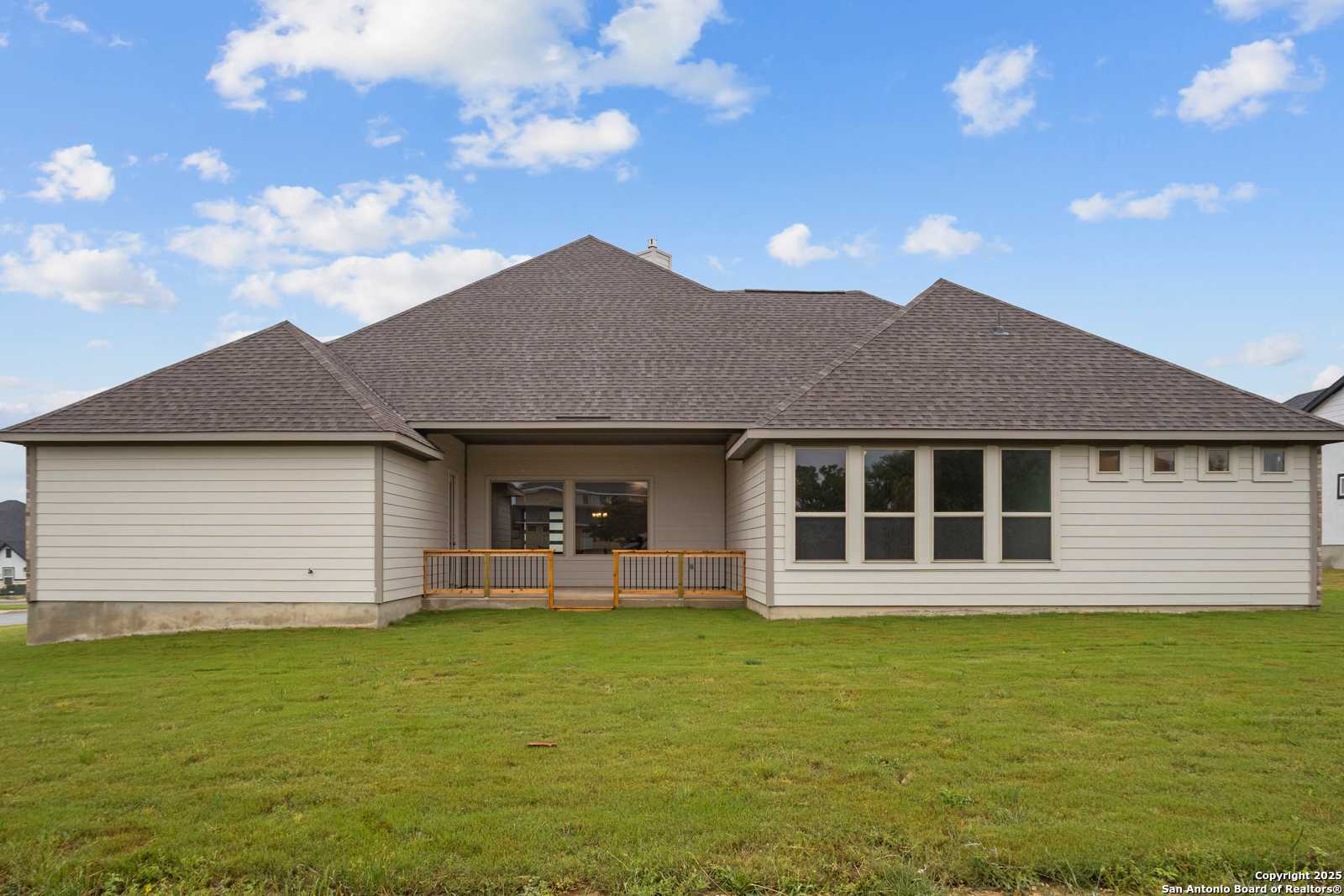 Rear view of Davidson Homes The Summerlin B single-story home with covered patio, large windows, and green lawn in Potranco Oaks, Castroville, Texas