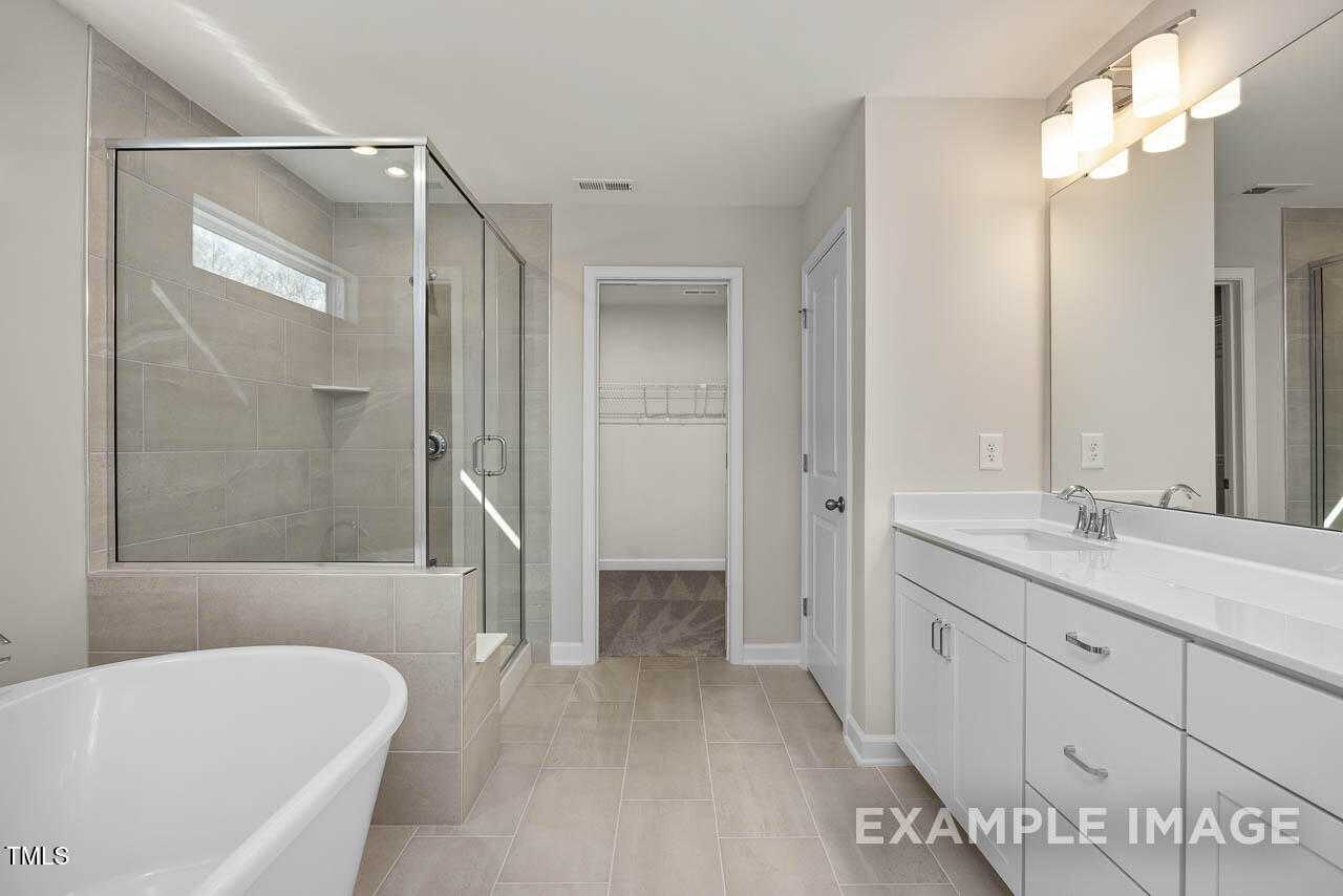 Modern master bathroom with freestanding tub, frameless glass shower, and double vanity in The Hickory II B, Lillington, NC