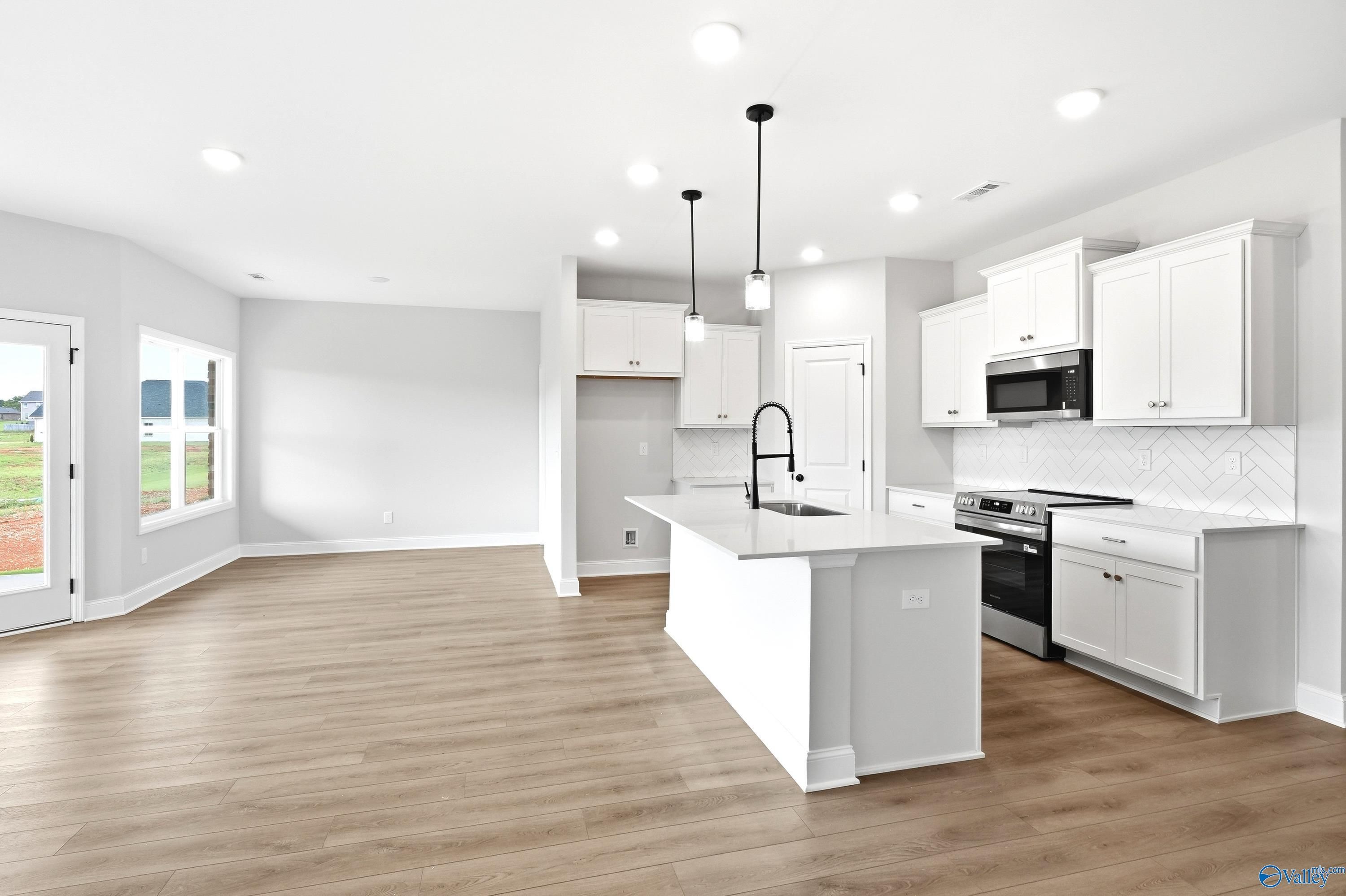 Modern kitchen with white cabinets, island, and herringbone backsplash in The Daphne floor plan, Lynn Meadows, Meridianville.