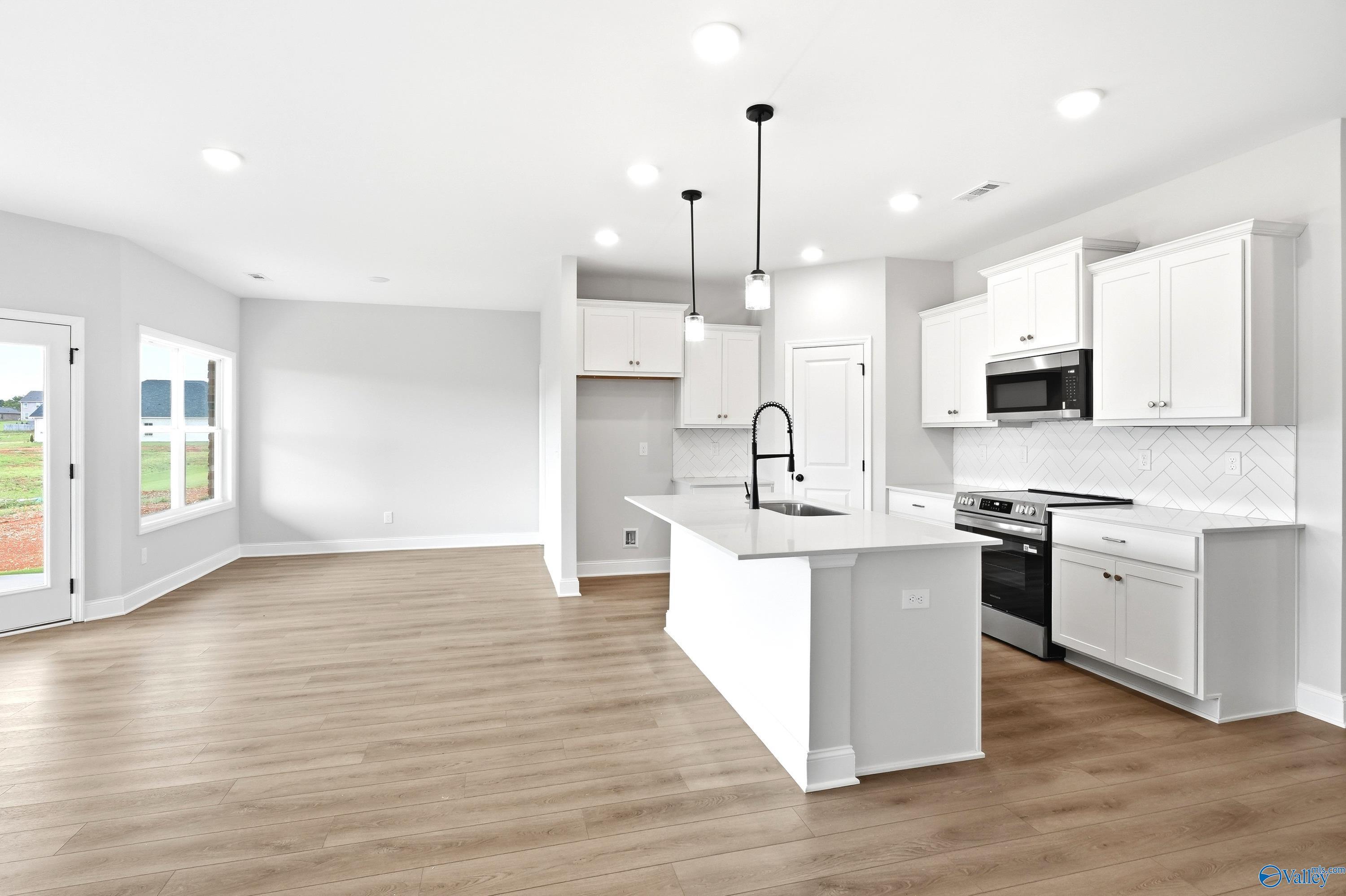 Modern kitchen with white cabinets, island, and herringbone backsplash in The Daphne floor plan, Lynn Meadows, Meridianville.