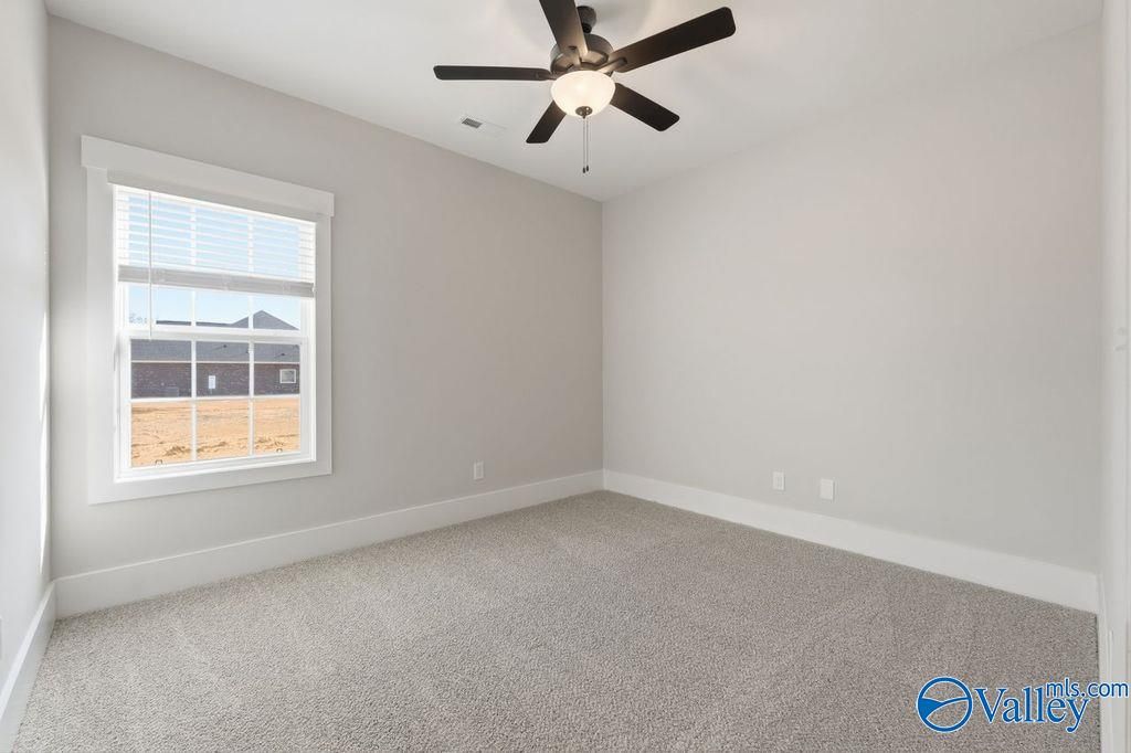 Bright bedroom with ceiling fan, gray walls, plush carpet, and window view in Davidson Homes The Rockford, Hartselle, Alabama