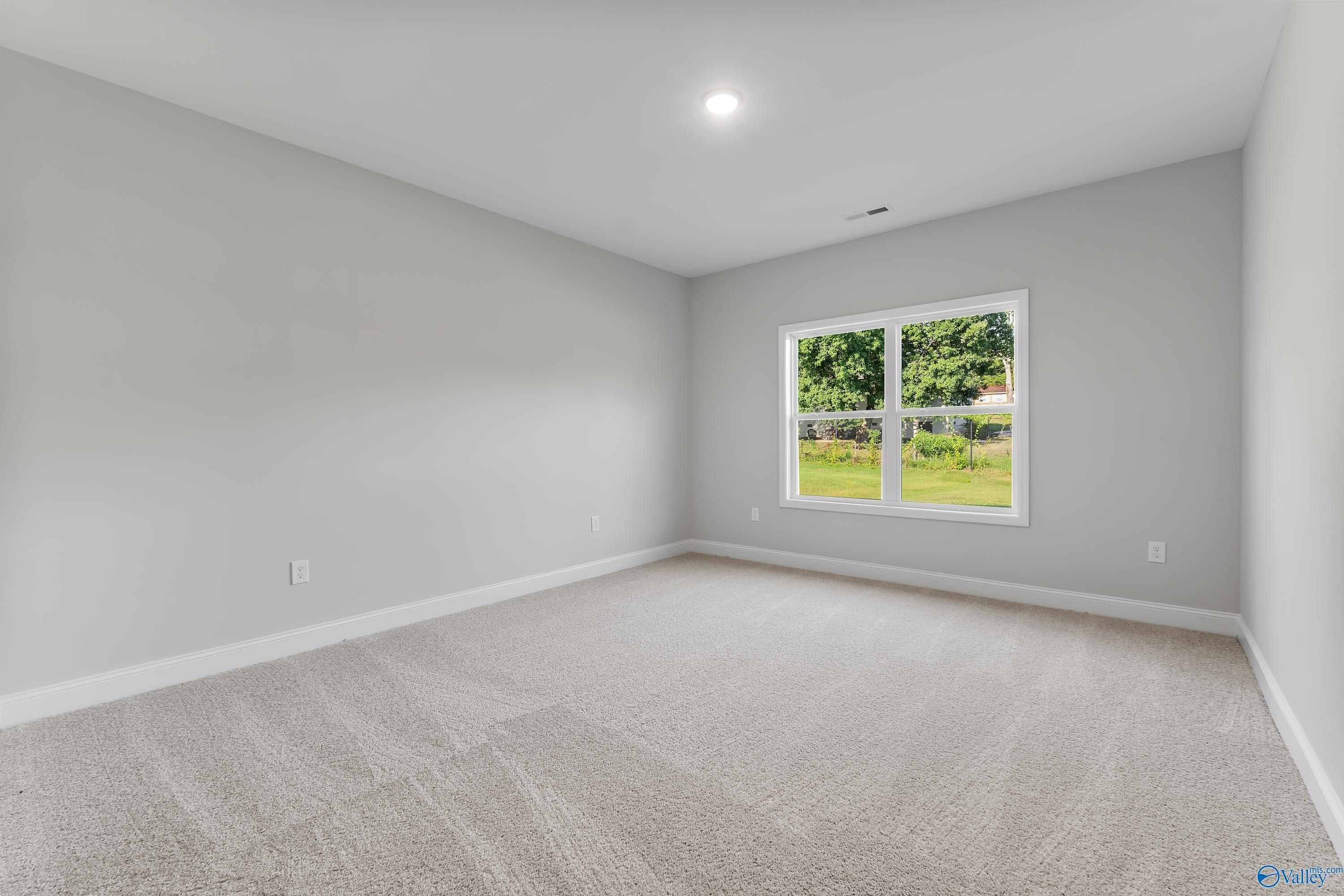 Bright empty bedroom with gray walls, neutral carpet, and large window to green yard in Davidson Homes The Daphne C, Huntsville AL