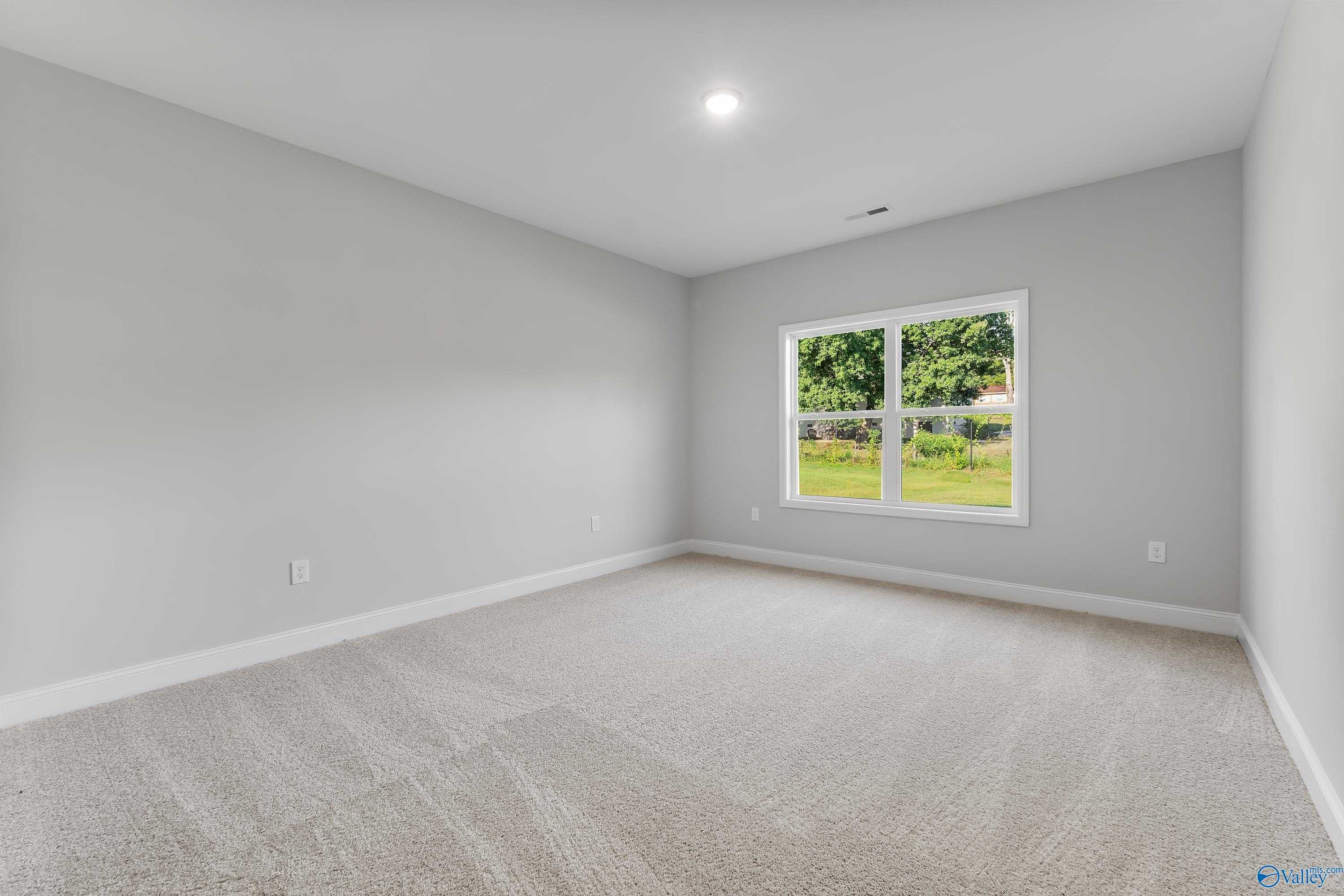 Bright empty bedroom with gray walls, neutral carpet, and large window to green yard in Davidson Homes The Daphne C, Huntsville AL