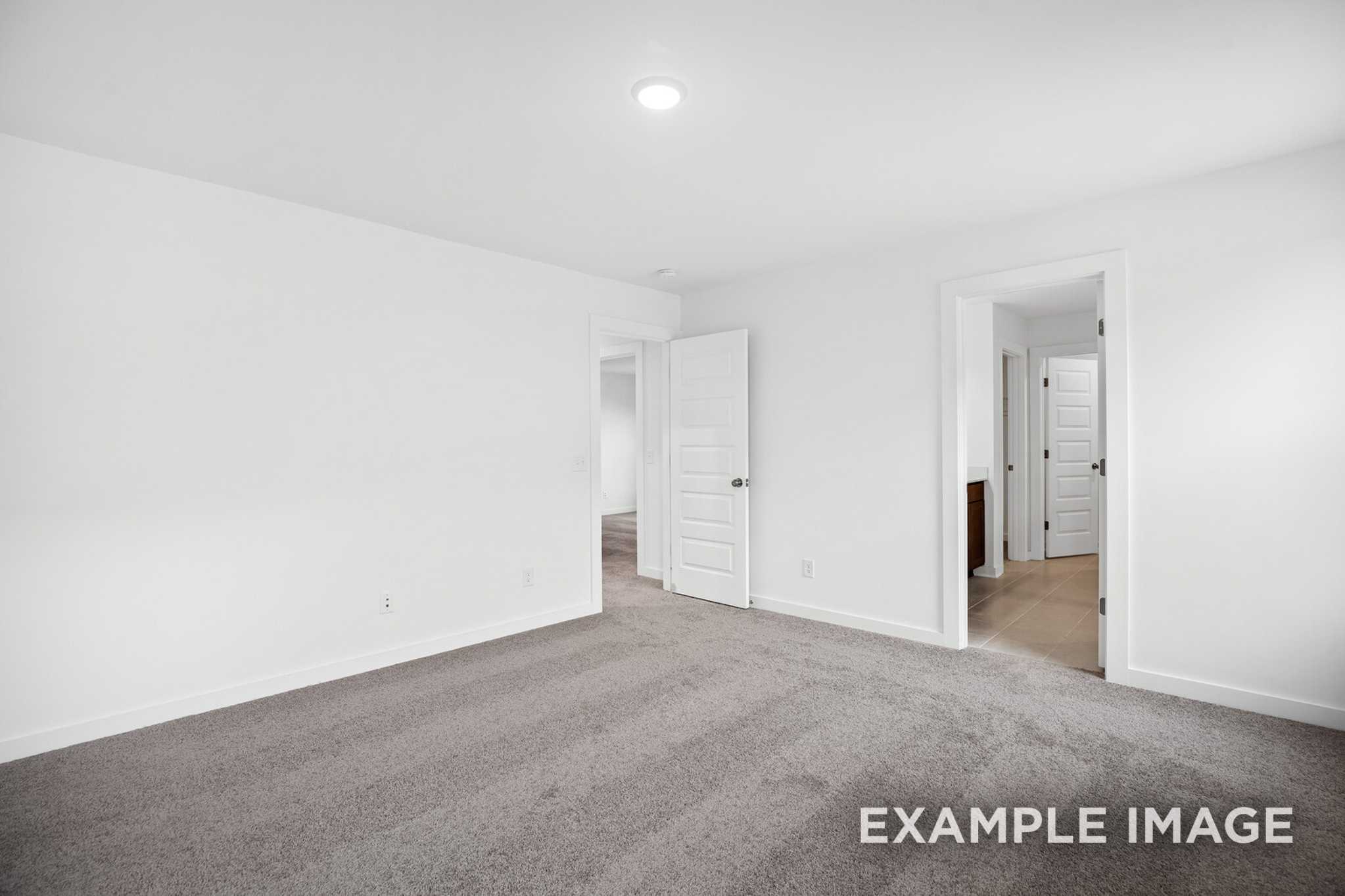 Spacious empty master bedroom in The Grayson C with white walls, gray carpet, recessed lighting, and doors to bath and closet