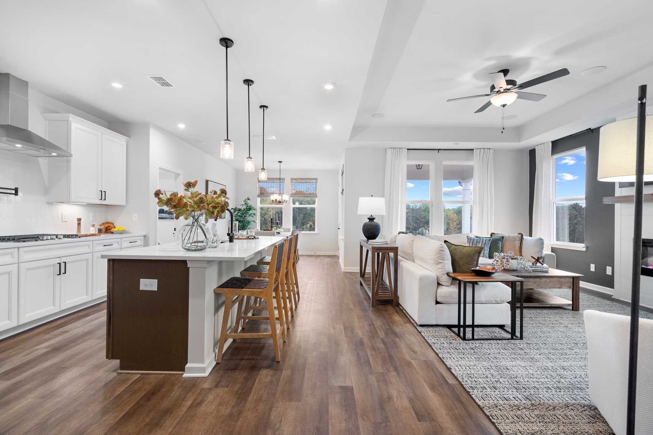 Open-concept kitchen and living room in The Edison C with white cabinets, large island, bar stools, and cozy sofa by Davidson Homes