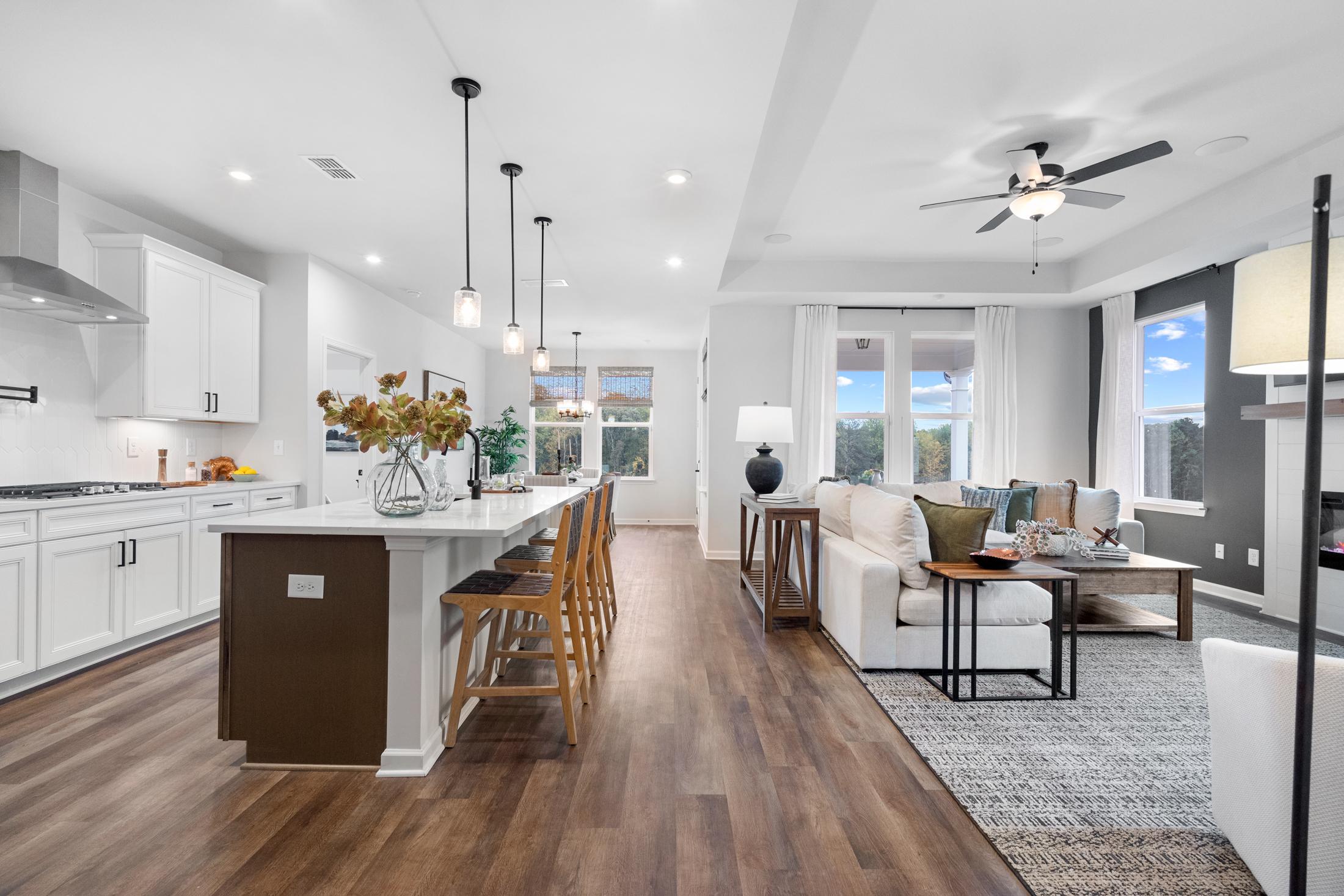 Open-concept kitchen and living room in The Edison home with white cabinets, large island, pendant lights, and cozy sofa
