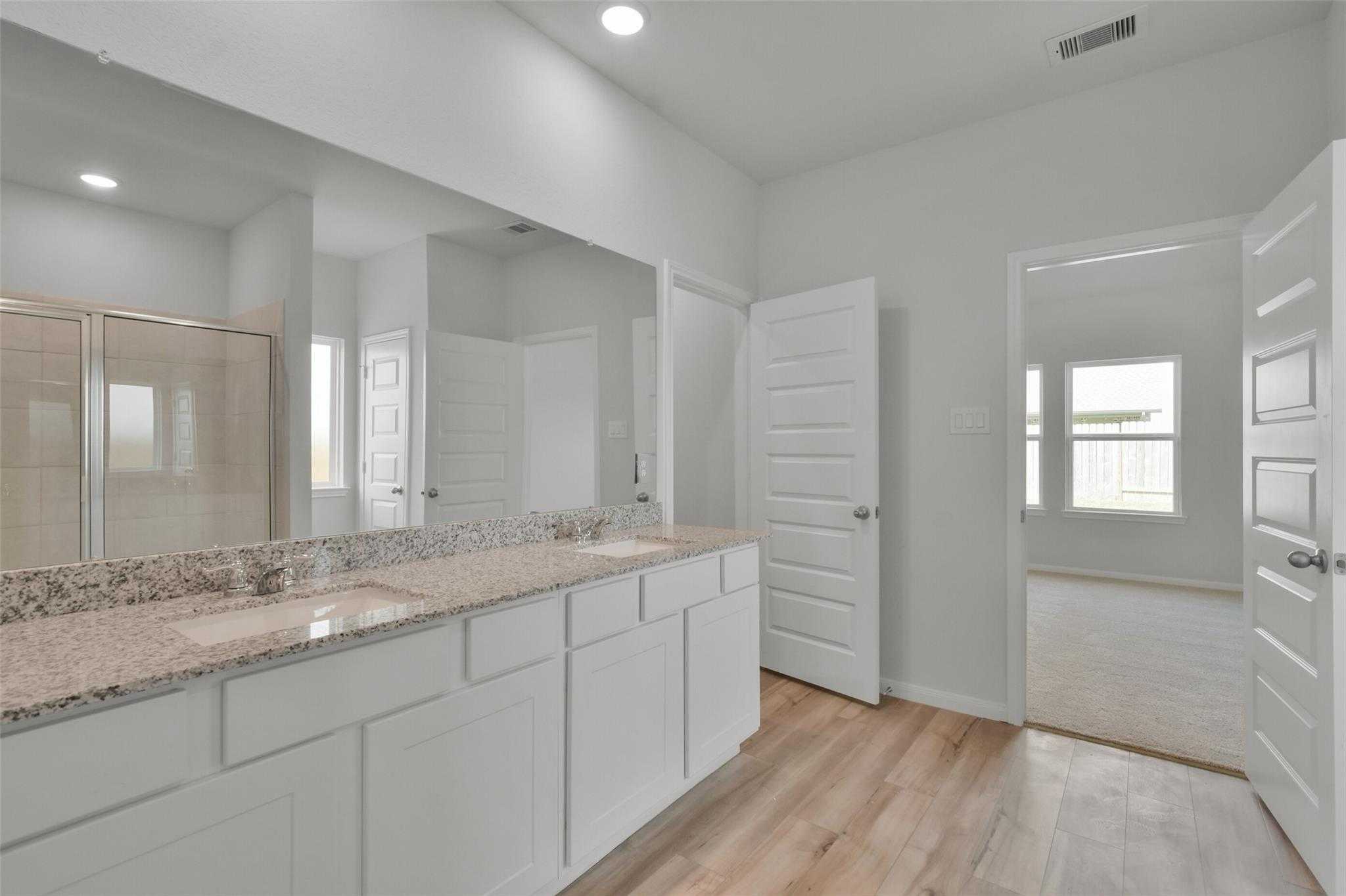 Modern master bathroom with double vanity, granite counters, glass shower, and hardwood floors in Davidson Homes The Tierra A, Dayton, Texas