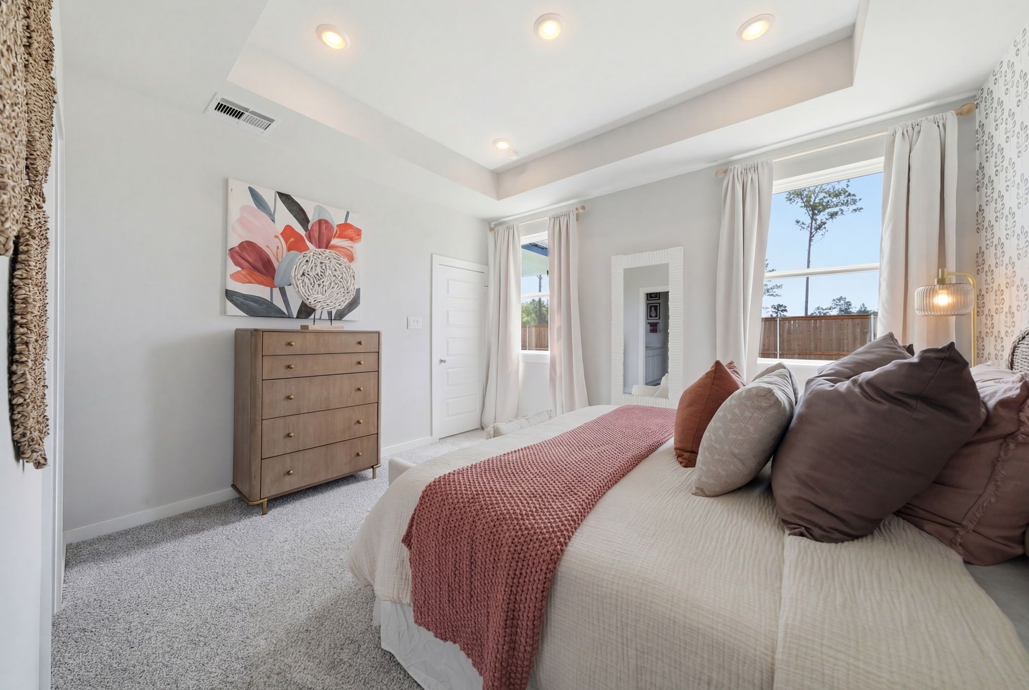 Spacious master bedroom at Spring Branch Crossing in Conroe Texas featuring king bed with red knit throw, wooden dresser, and abstract floral art