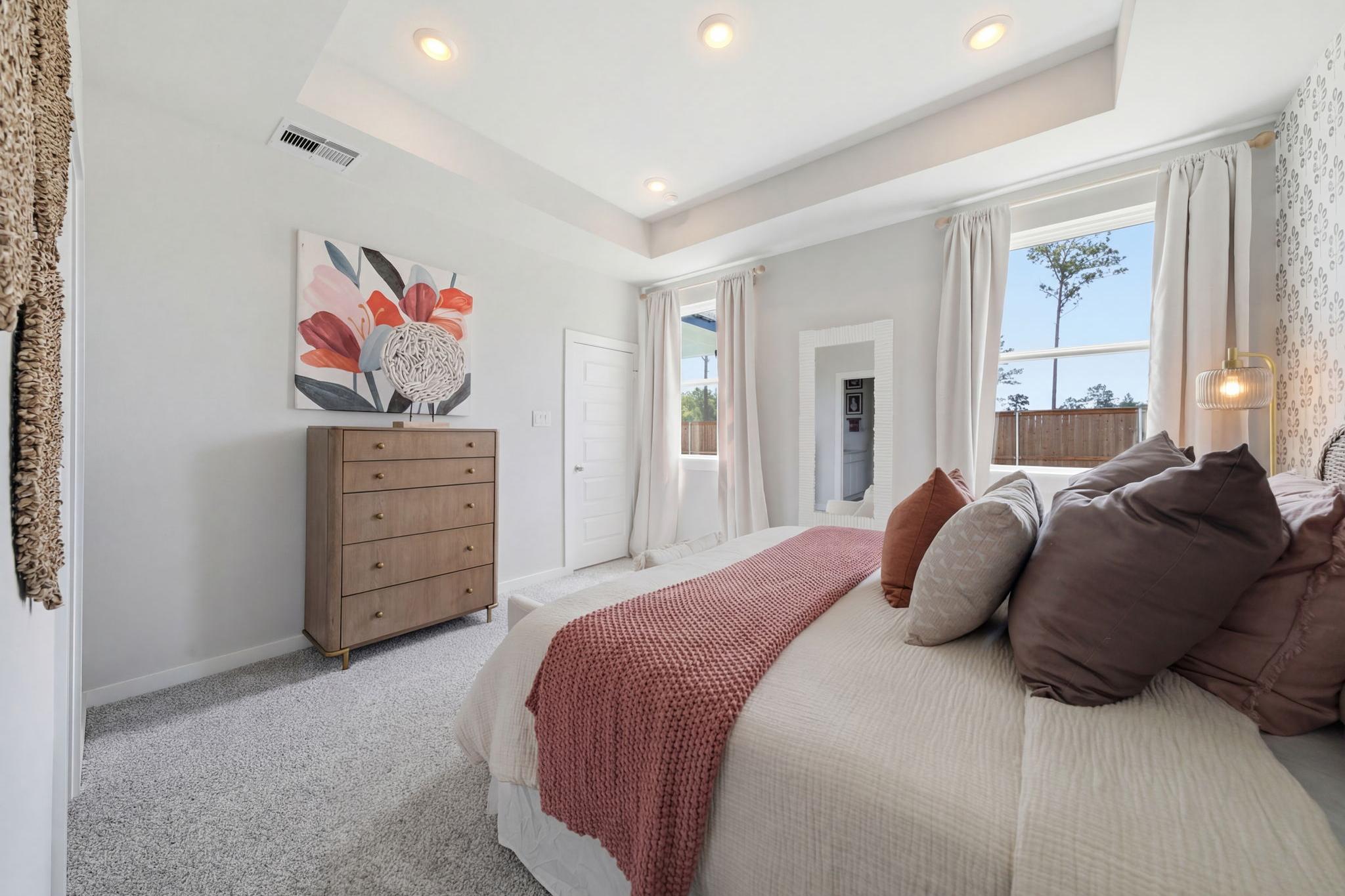Spacious master bedroom at Spring Branch Crossing in Conroe Texas featuring king bed with red knit throw, wooden dresser, and abstract floral art