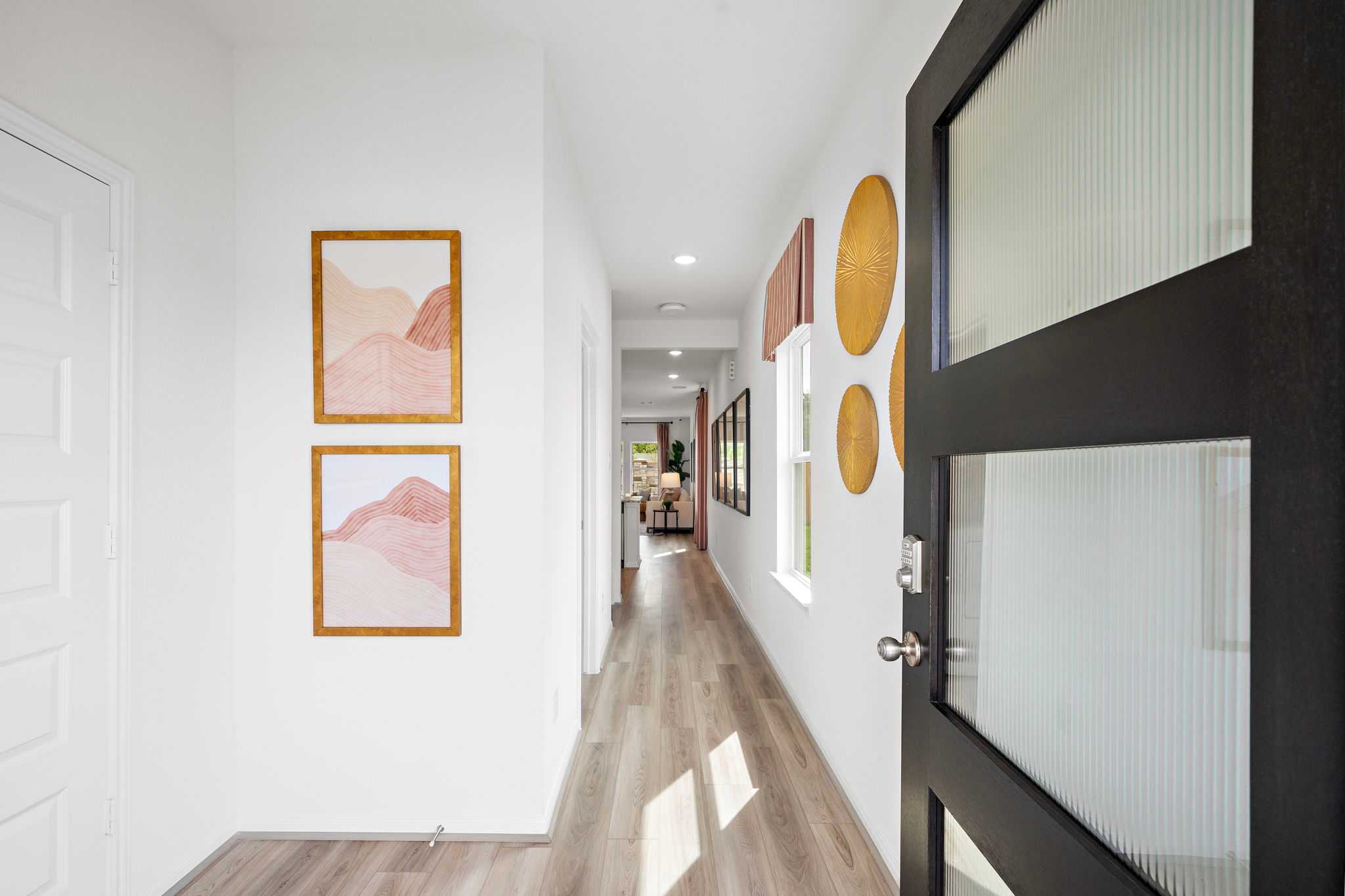 Spacious hallway interior at The Villages at WestPointe in Dayton Texas with light wood floors, pink abstract art, and frosted glass door