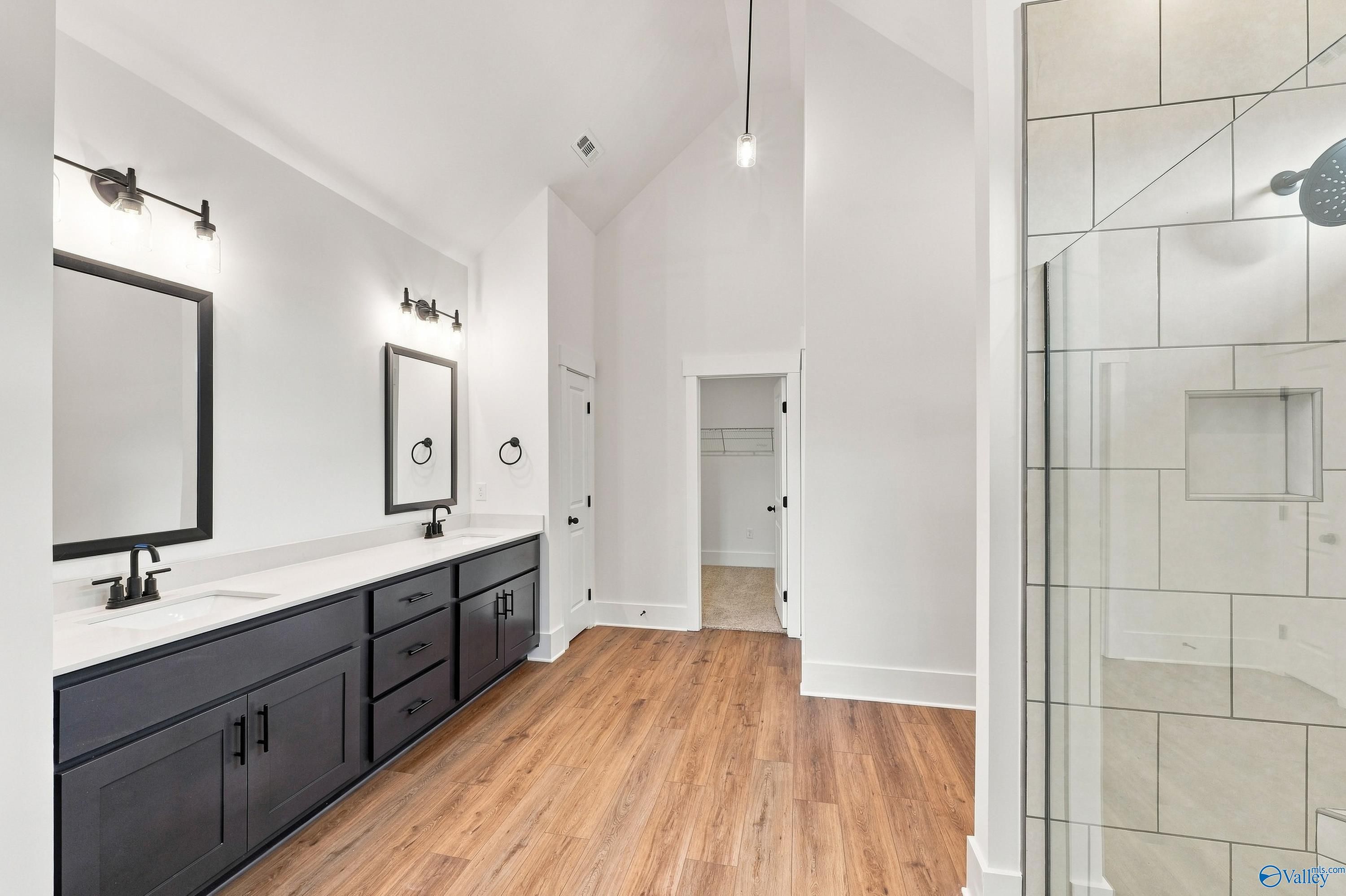 Primary bathroom with dark double vanity, walk-in tile shower, and hardwood floors in The Valencia, Huntsville, Alabama