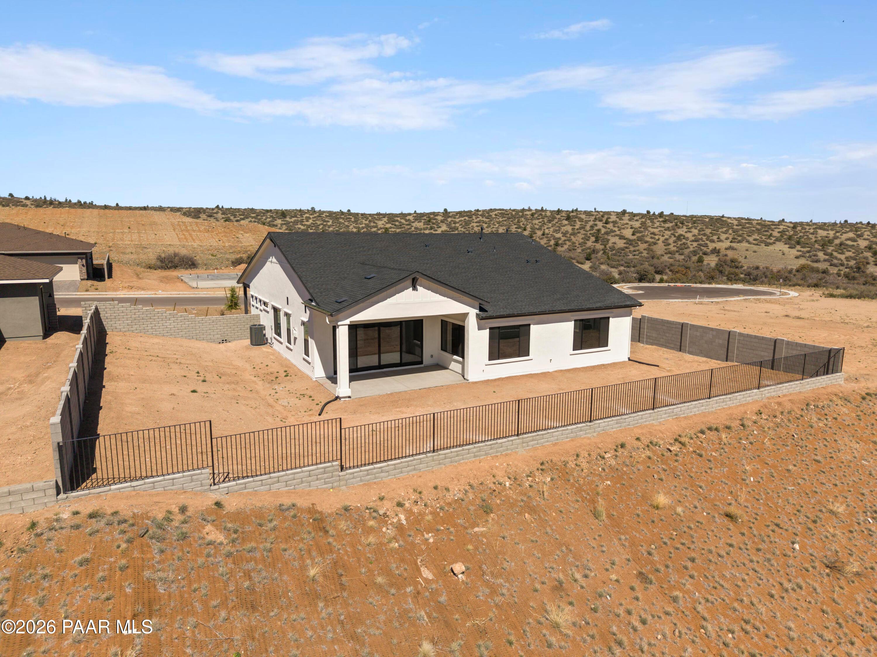 Aerial view of modern single-story Soleil E home with white stucco exterior, black roof, 3-car garage, and fenced yard in Hidden Hills, Prescott, Arizona