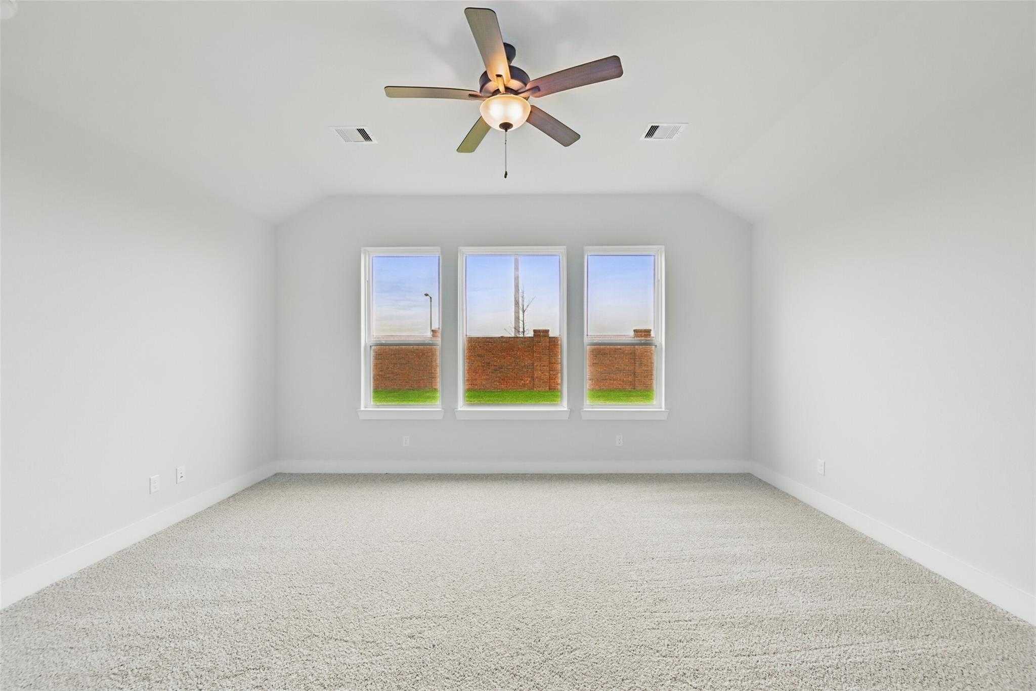 Bright empty room with lighted ceiling fan and triple windows overlooking brick home and lawn in Davidson Homes The Victoria C, Lago Mar