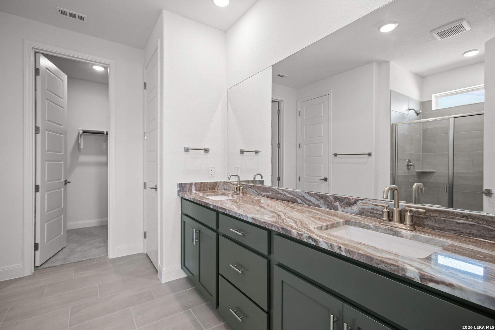 Modern primary bathroom with double vanity, stone countertop, and walk-in closet in The Lanier G home, Castroville, TX.